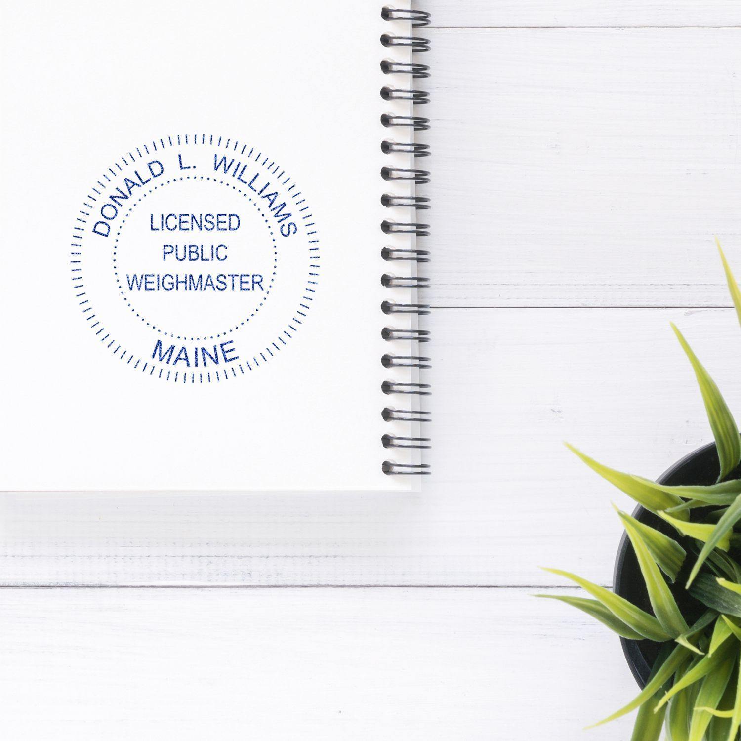 Xstamper Public Weighmaster Pre-Inked Rubber Stamp of Seal used on a white notebook, next to a green plant on a white wooden desk.