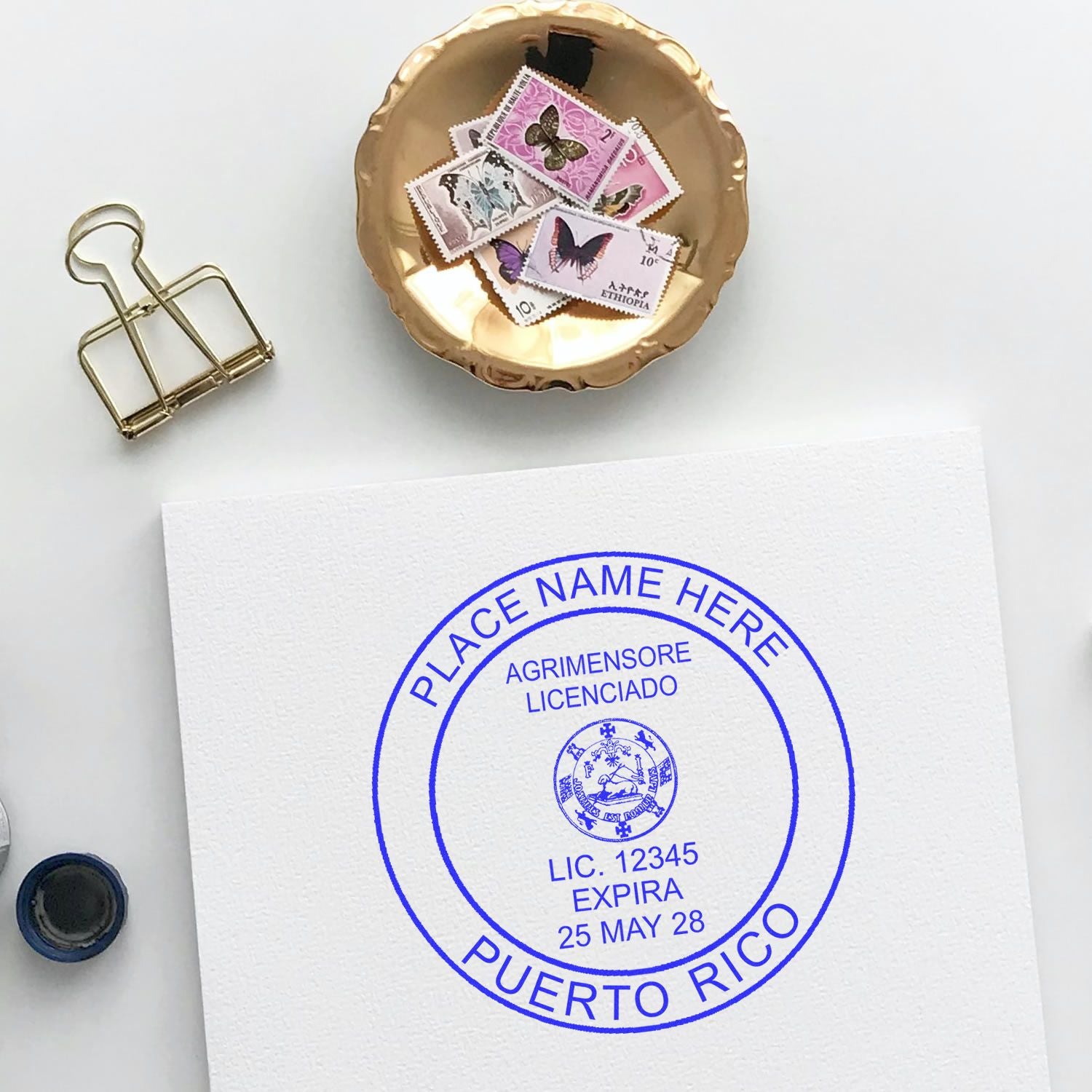 Self Inking Puerto Rico Land Surveyor Stamp in blue ink on white paper, surrounded by stamps, a clip, and a gold dish.