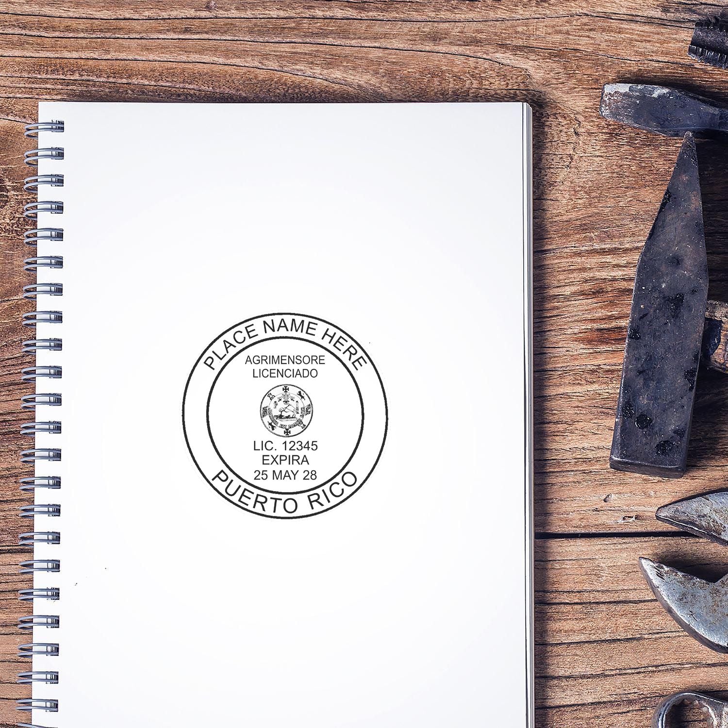 Puerto Rico Land Surveyor Seal Stamp on a white notebook, surrounded by tools on a wooden surface.