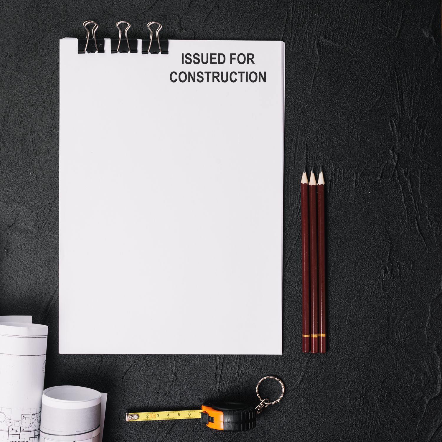 A blank sheet with a Regular Issued for Construction Stamp at the top, surrounded by pencils, a tape measure, and blueprints.