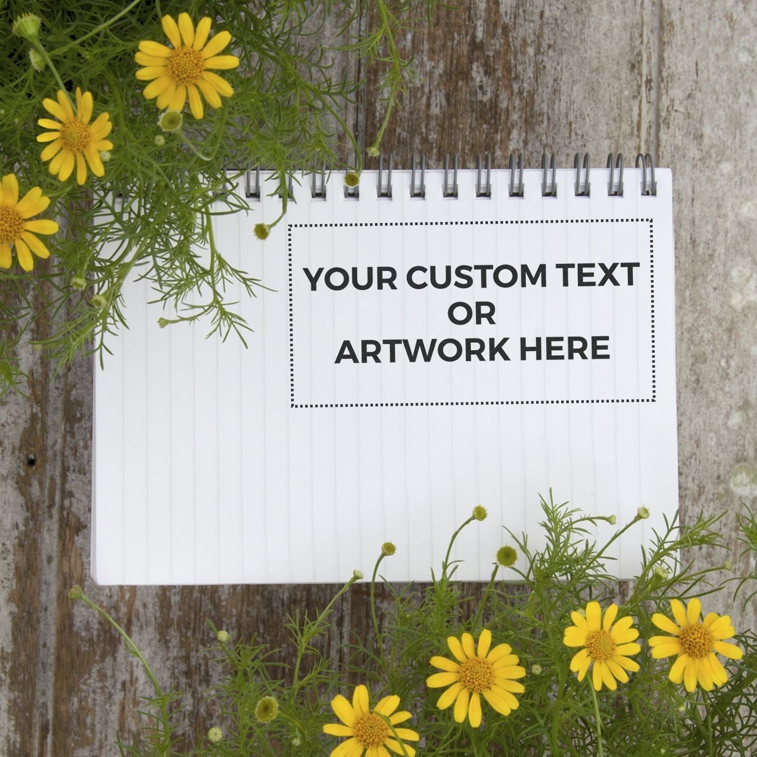 Custom Rubber Stamp Size 3 x 6 stamped on a spiral notebook page surrounded by yellow flowers on a wooden surface.