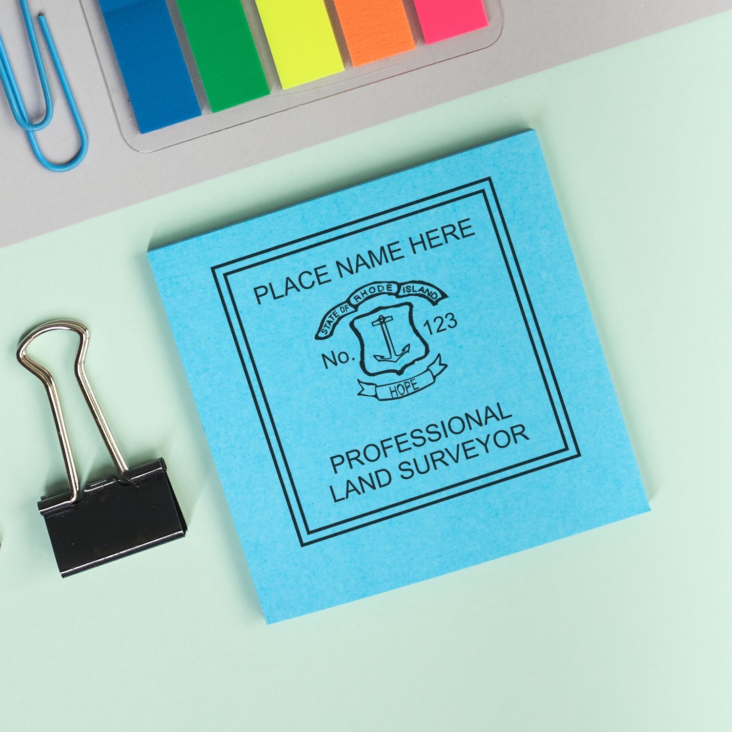 Rhode Island Land Surveyor Seal Stamp on blue paper, surrounded by colorful sticky notes, paper clips, and a binder clip.