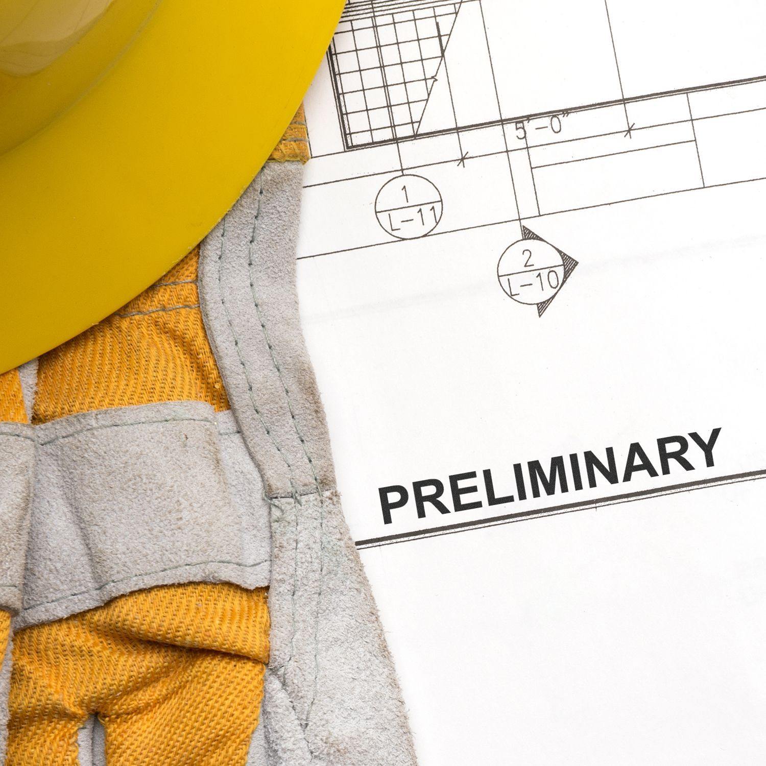 Self Inking Preliminary Stamp used on a construction blueprint with a yellow hard hat and safety gloves nearby.