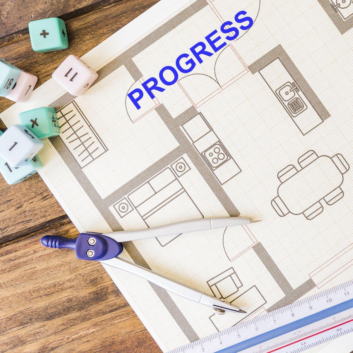 Self Inking Progress Stamp marking PROGRESS on a floor plan, surrounded by drafting tools and dice on a wooden table.