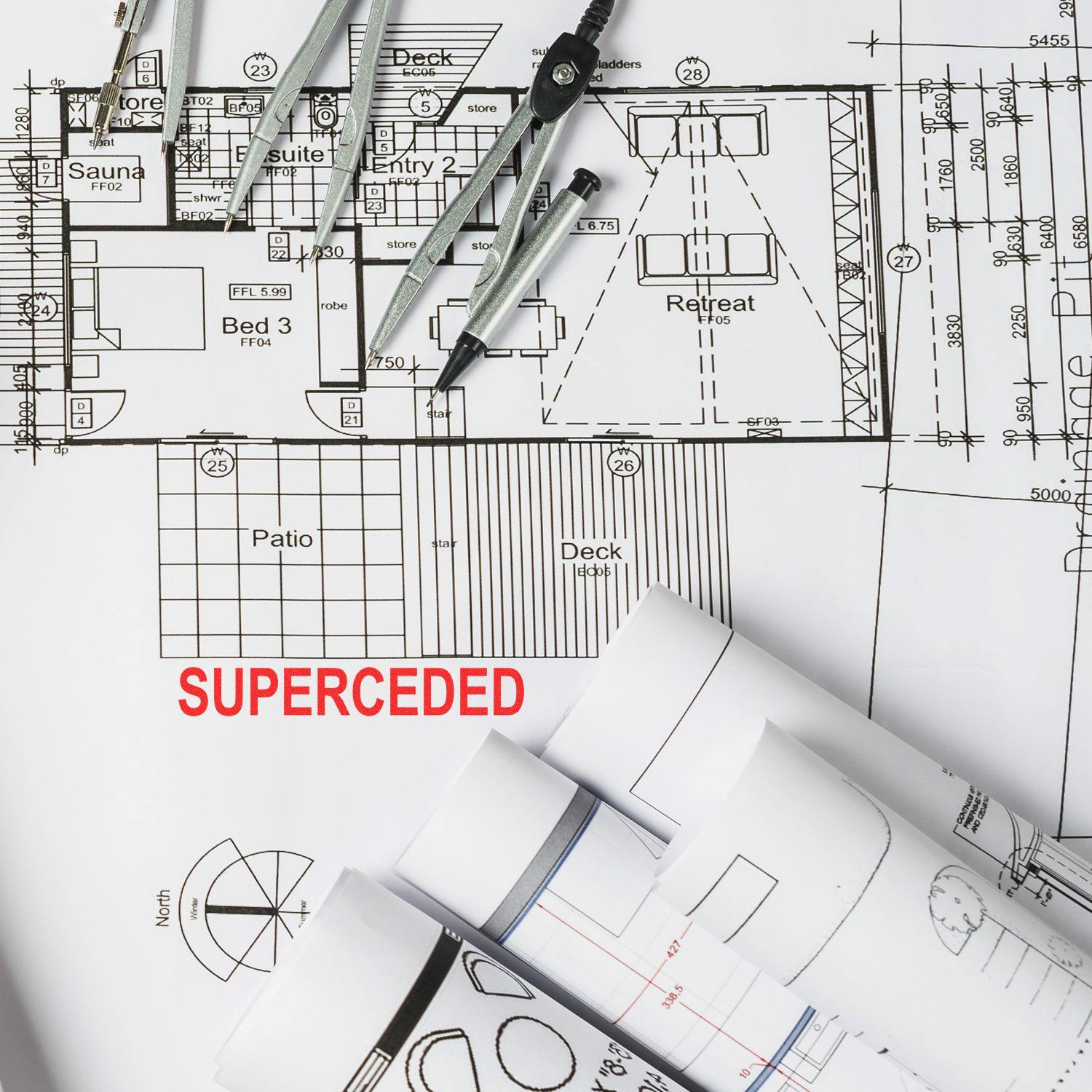 Blueprint with SUPERCEDED stamped in red using a Self Inking Superceded Stamp, surrounded by drafting tools and rolled-up plans.