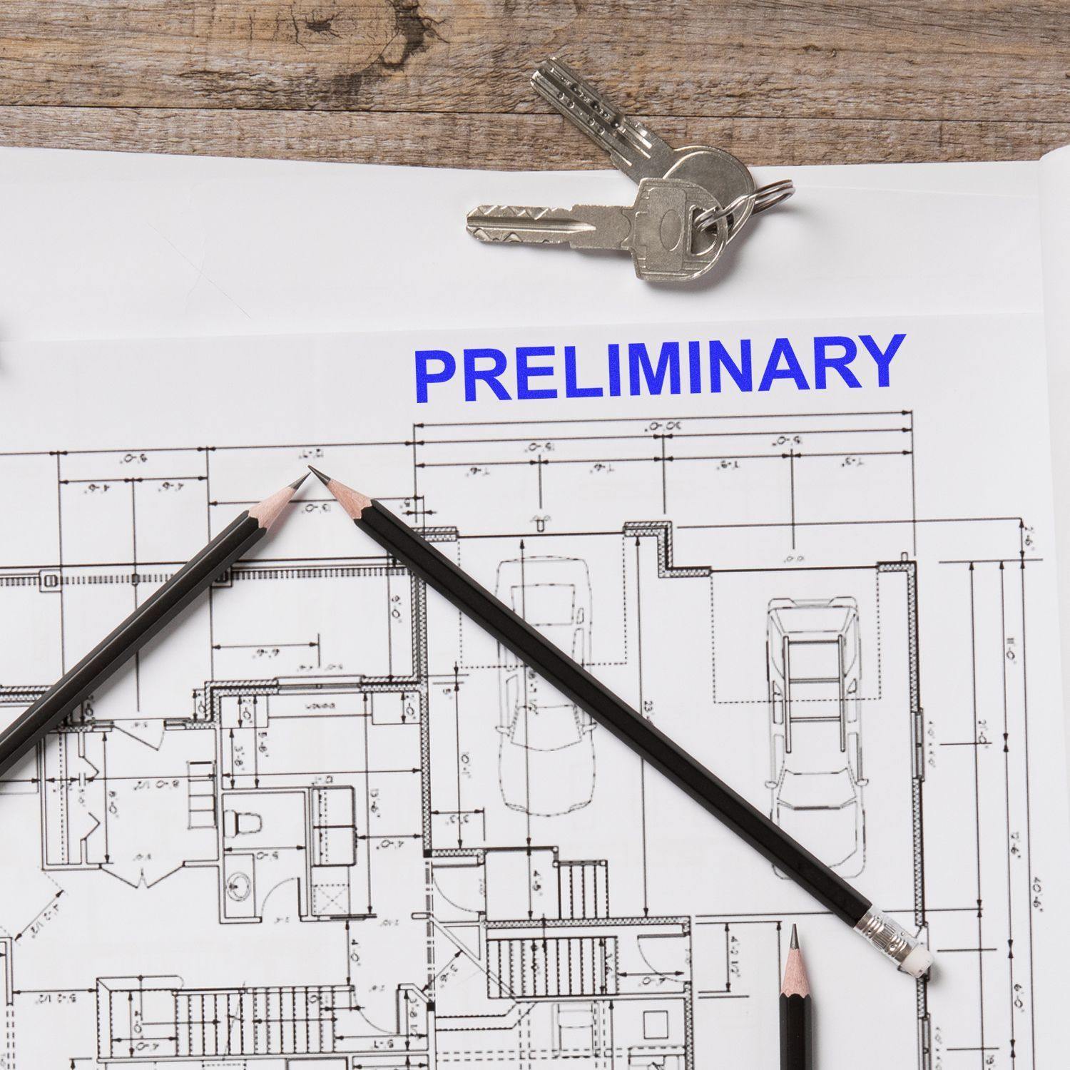 Slim Pre-Inked Preliminary Stamp marking a blueprint with the word PRELIMINARY in blue ink, surrounded by pencils and keys.