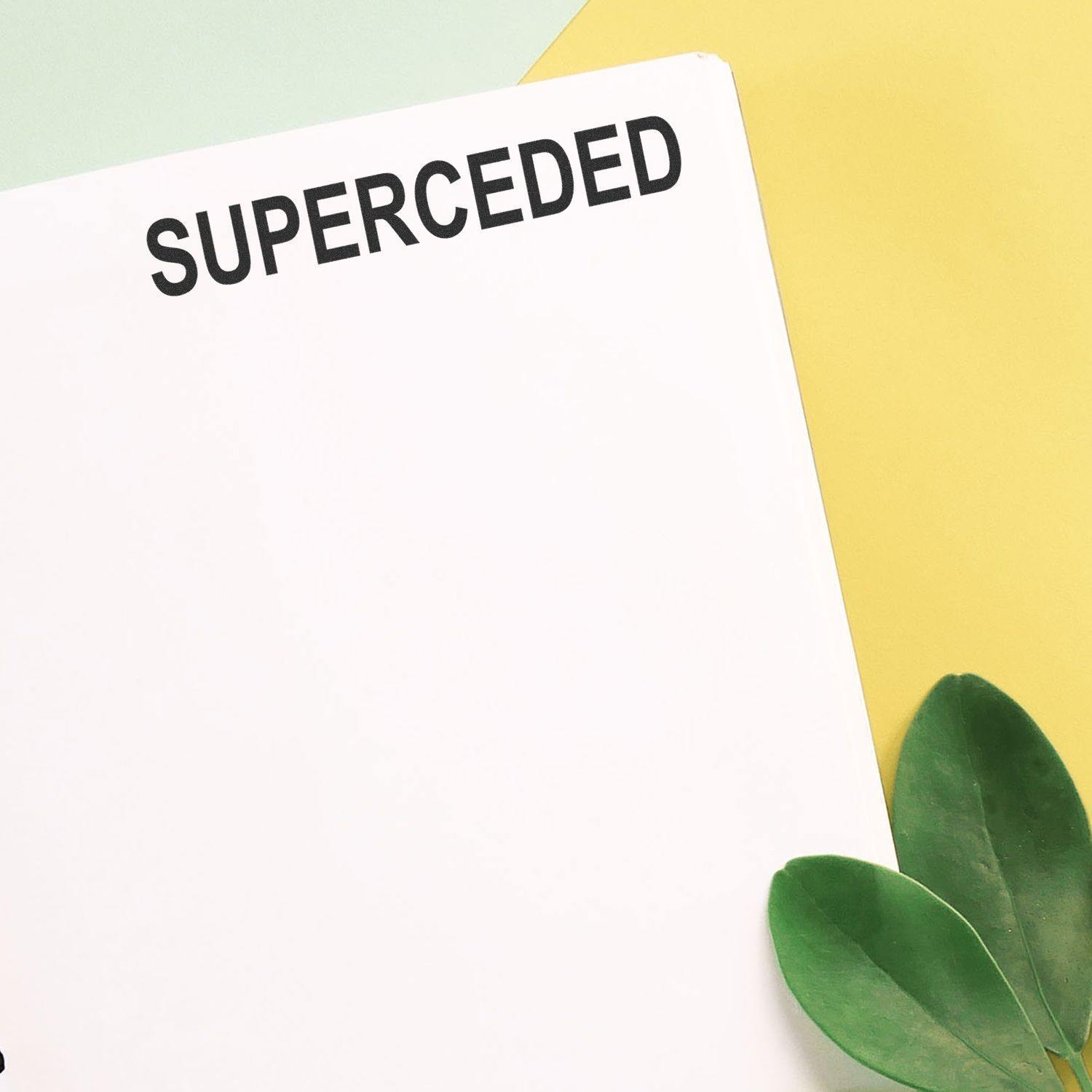 Slim Pre-Inked Superceded Stamp marking SUPERCEDED on white paper, with green leaves and pastel yellow and green background.