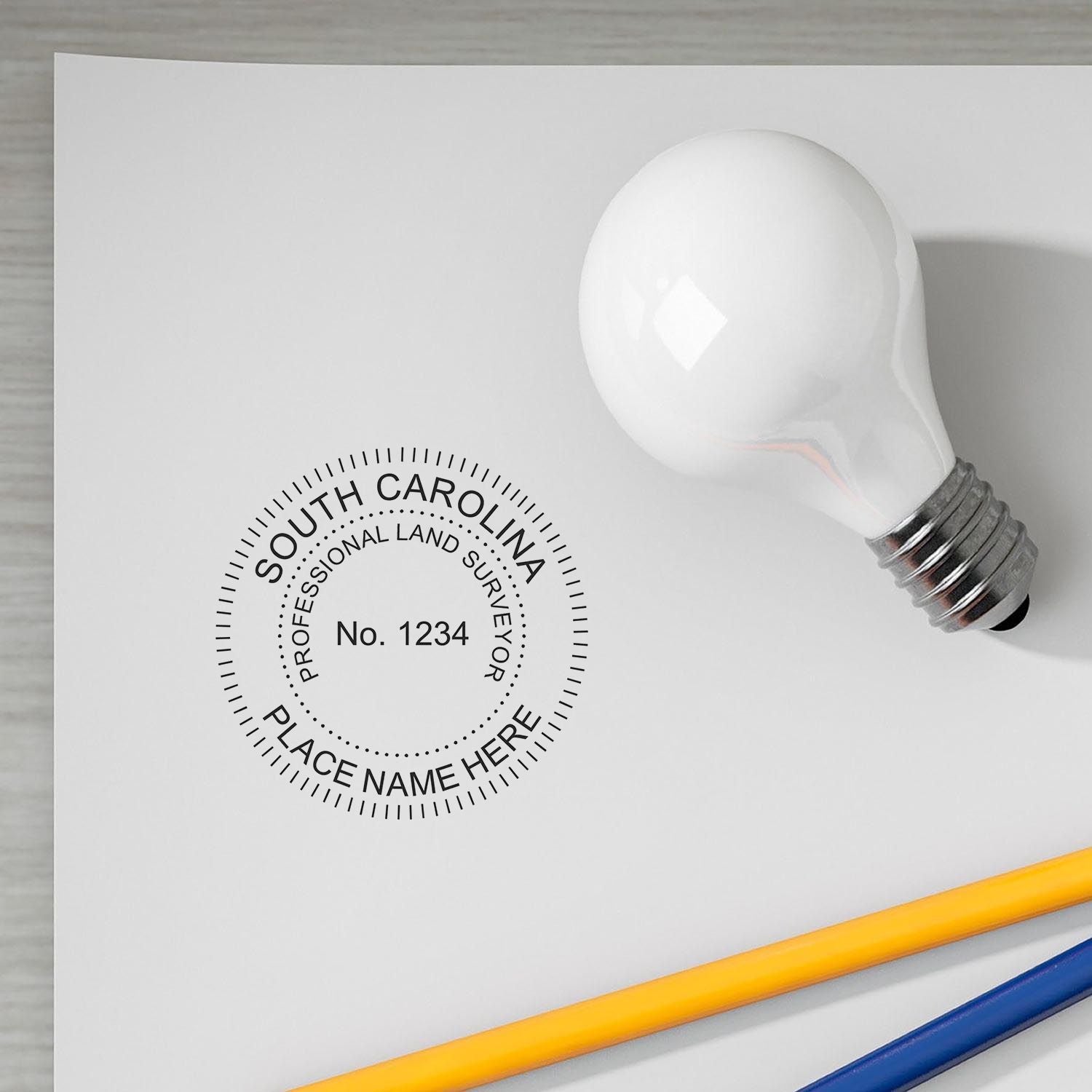 Digital South Carolina Land Surveyor Stamp, Electronic Seal for South Carolina Land Surveyor on paper with a light bulb and pencils nearby.