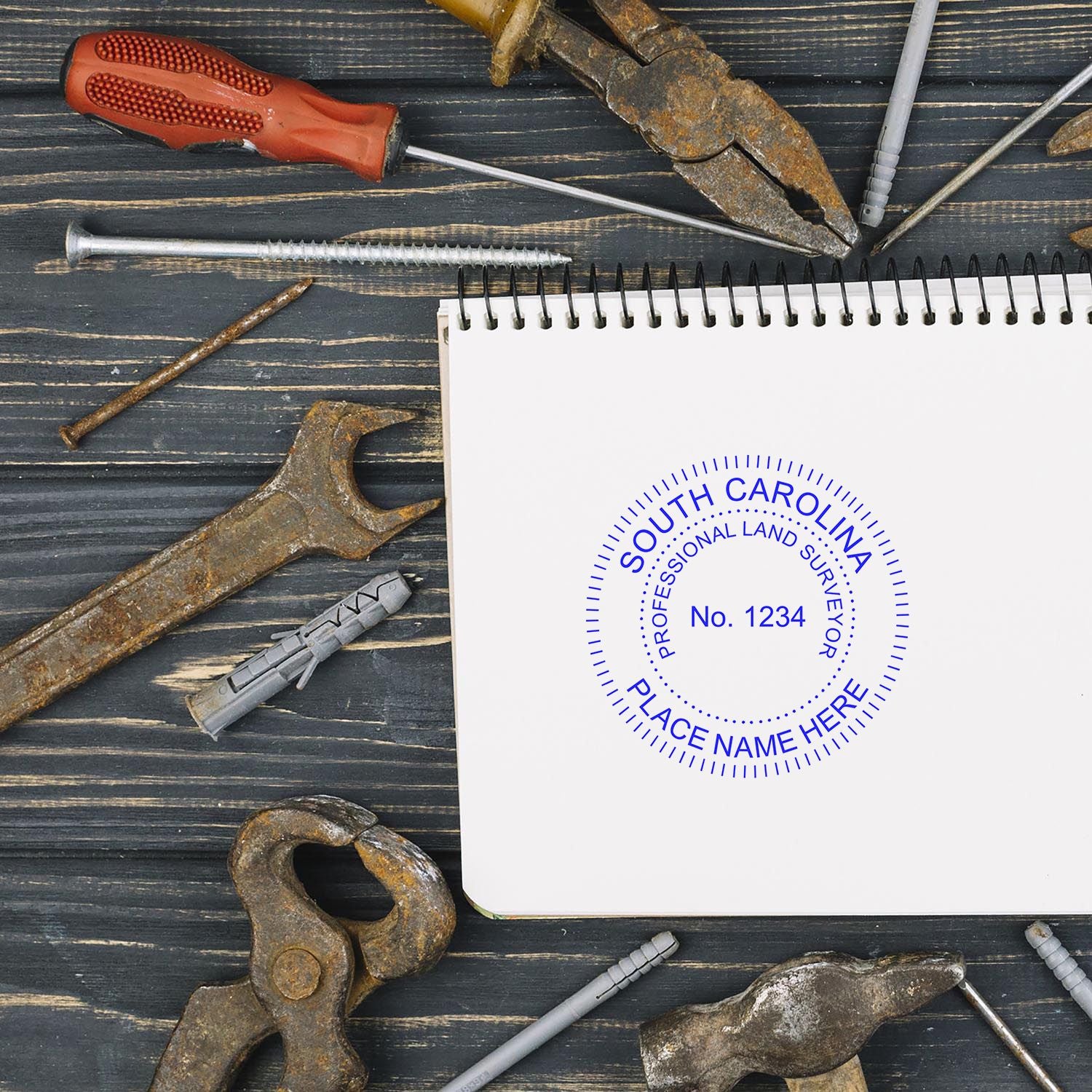 Self Inking South Carolina Land Surveyor Stamp on a notebook surrounded by various tools on a wooden surface.