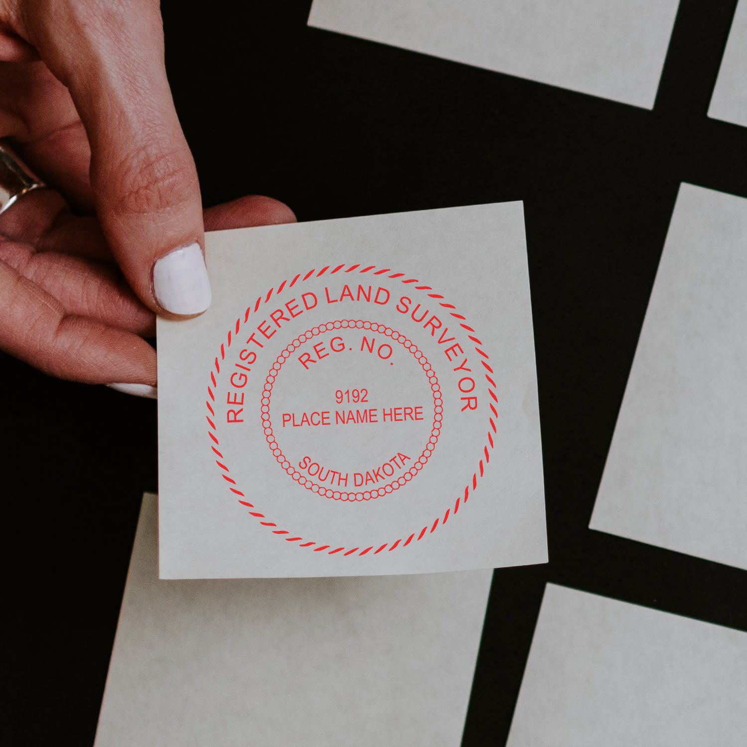 Hand holding a stamped paper with the Premium MaxLight Pre-Inked South Dakota Surveyors Stamp, displaying Registered Land Surveyor text.