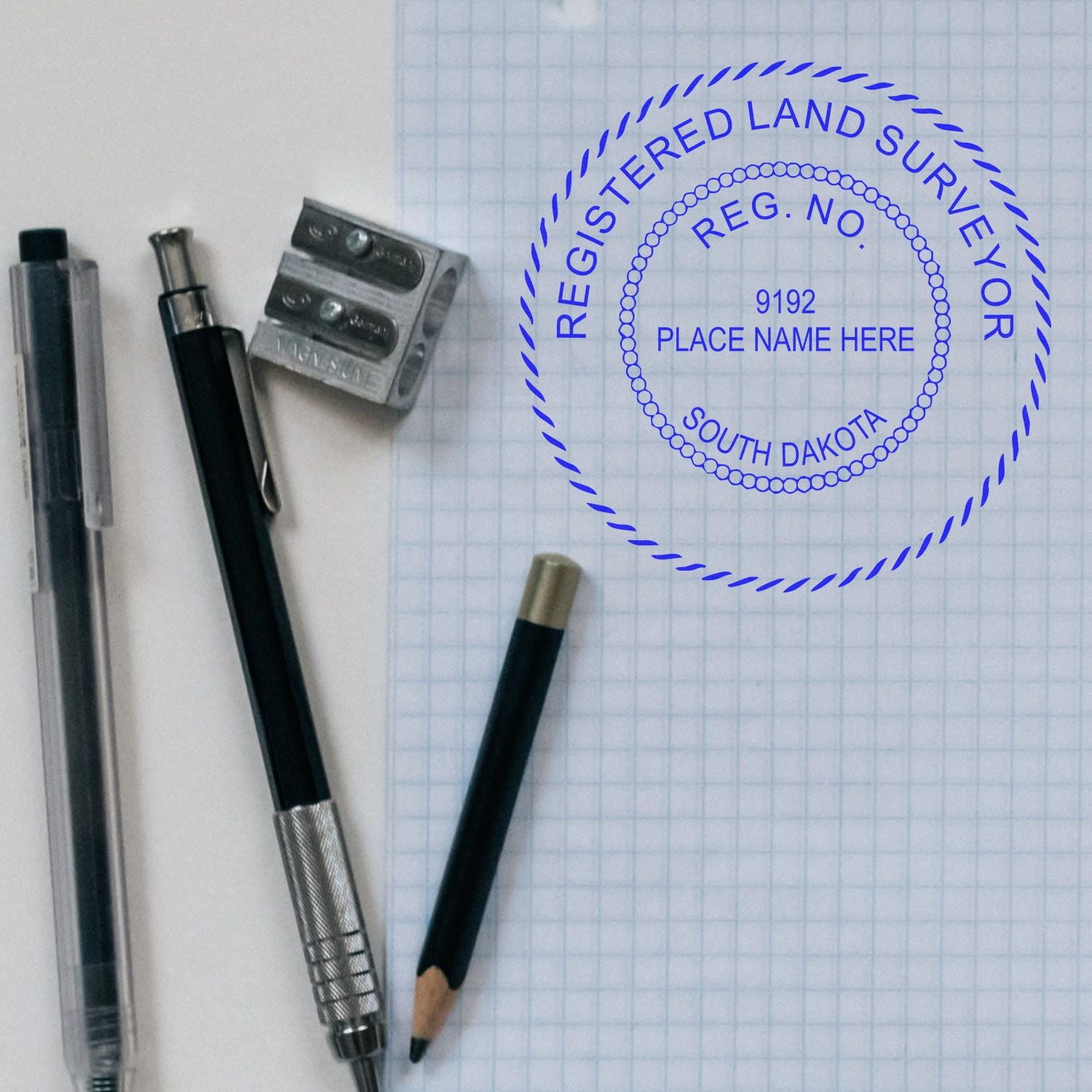 Self Inking South Dakota Land Surveyor Stamp on graph paper with pen, pencil, and sharpener nearby.