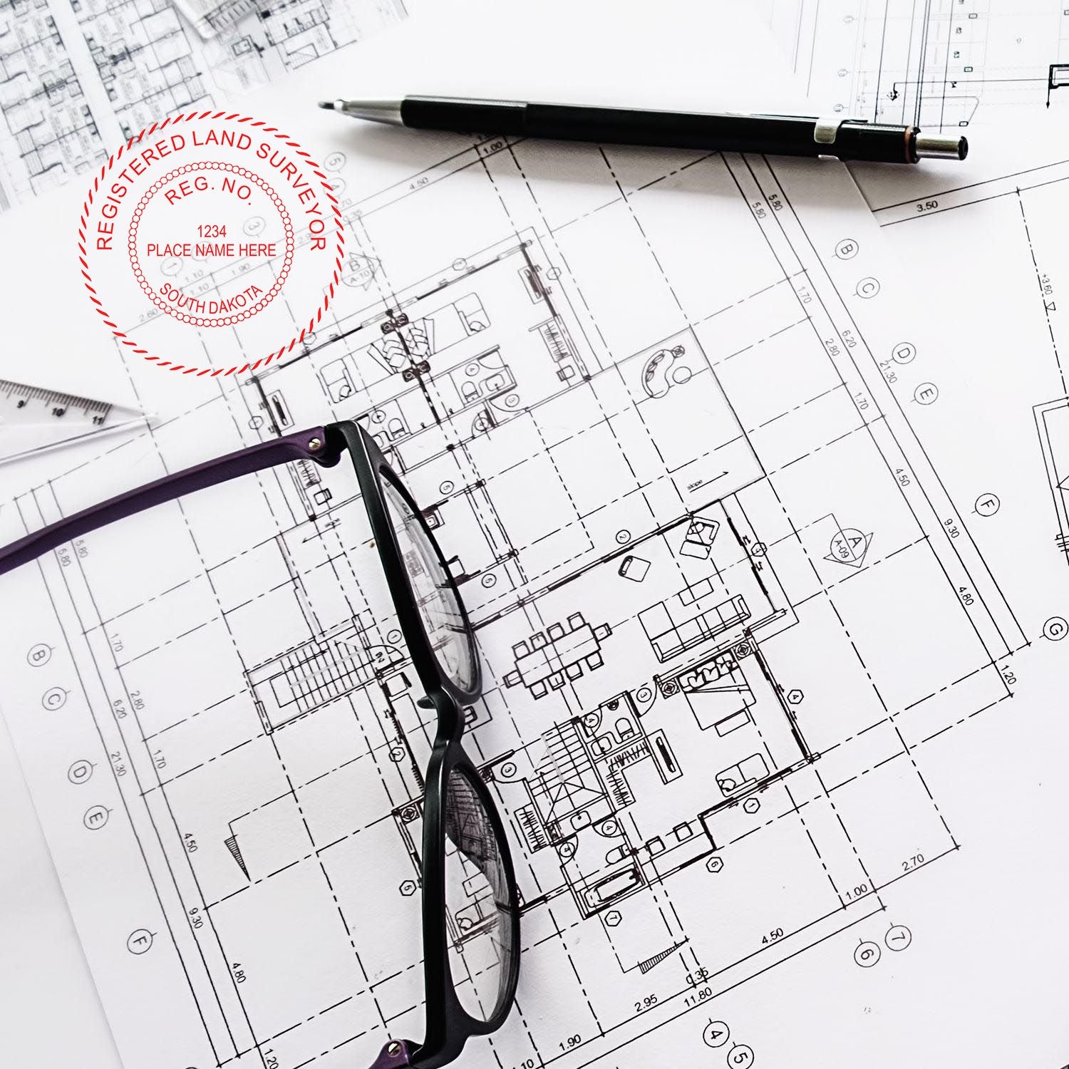 South Dakota Land Surveyor Seal Stamp on architectural blueprints with a pen and glasses placed on top.