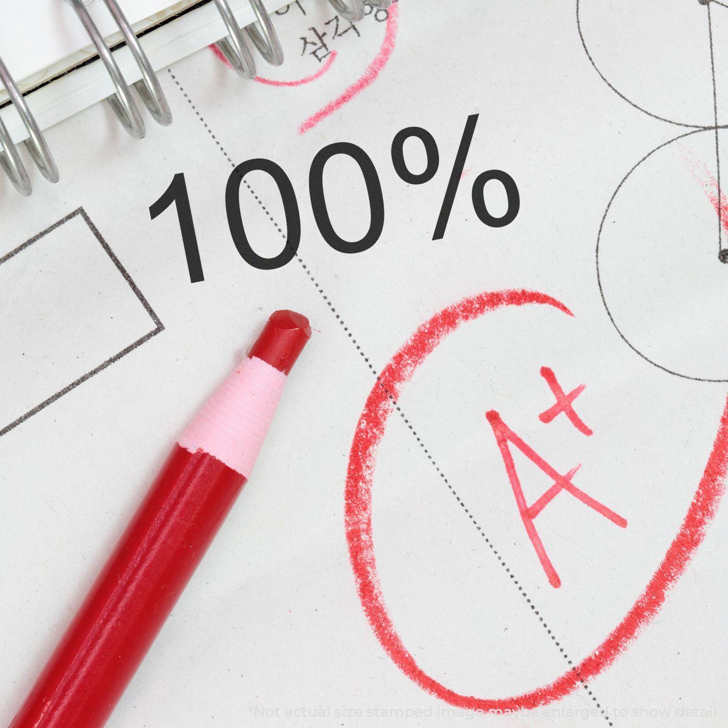 A red pen circles an A+ on a paper next to a stamped 100% using the Self Inking 100% Stamp, with a notebook in the background.