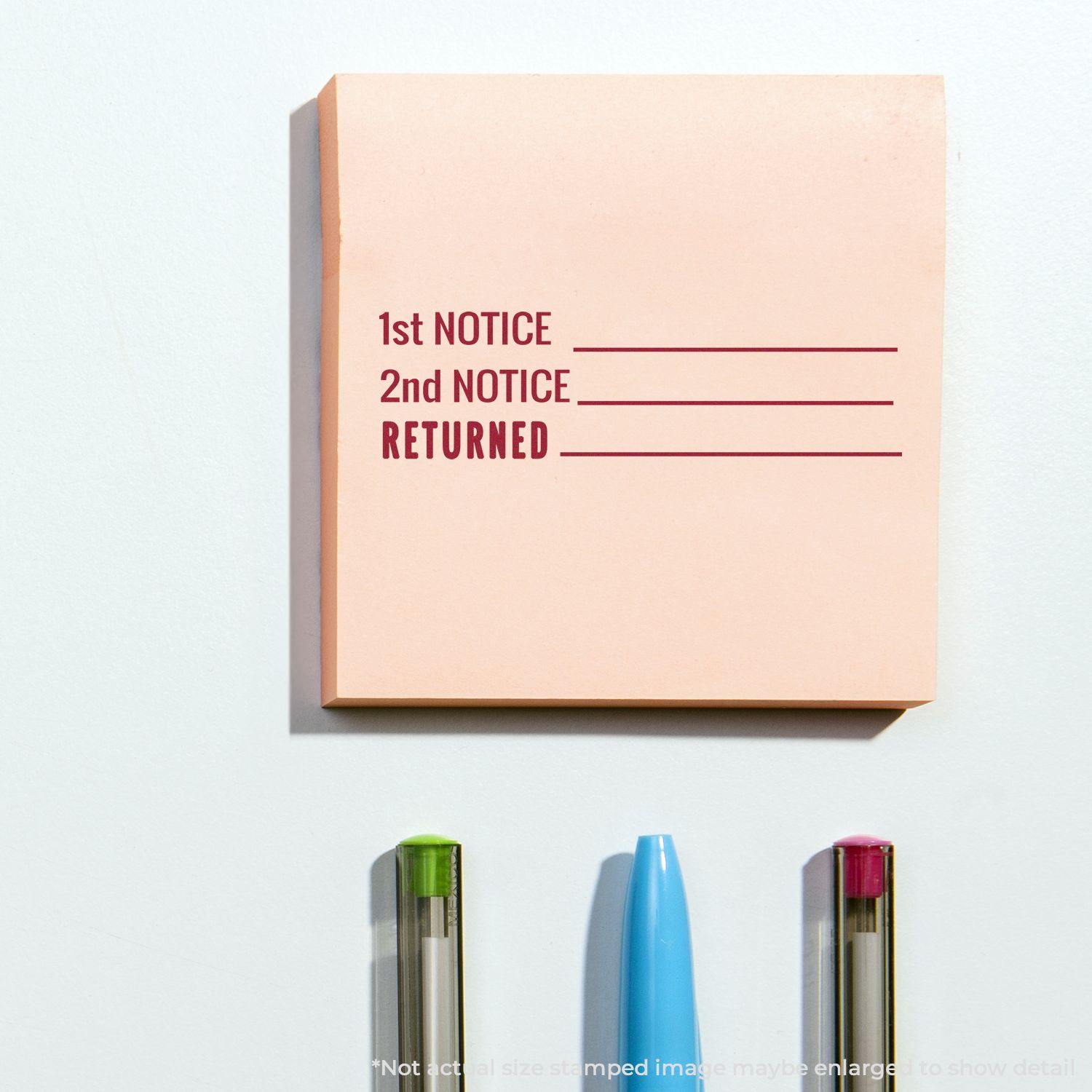 Self Inking 1st 2nd Notice Returned Stamp used on a pink sticky note, with three pens below it on a white surface.