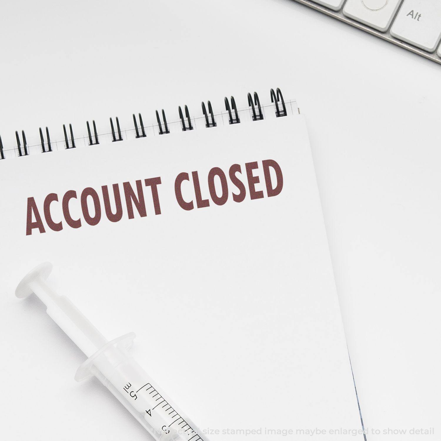 A Self Inking Account Closed Stamp marks ACCOUNT CLOSED in red on a white notepad, with a syringe and keyboard nearby.