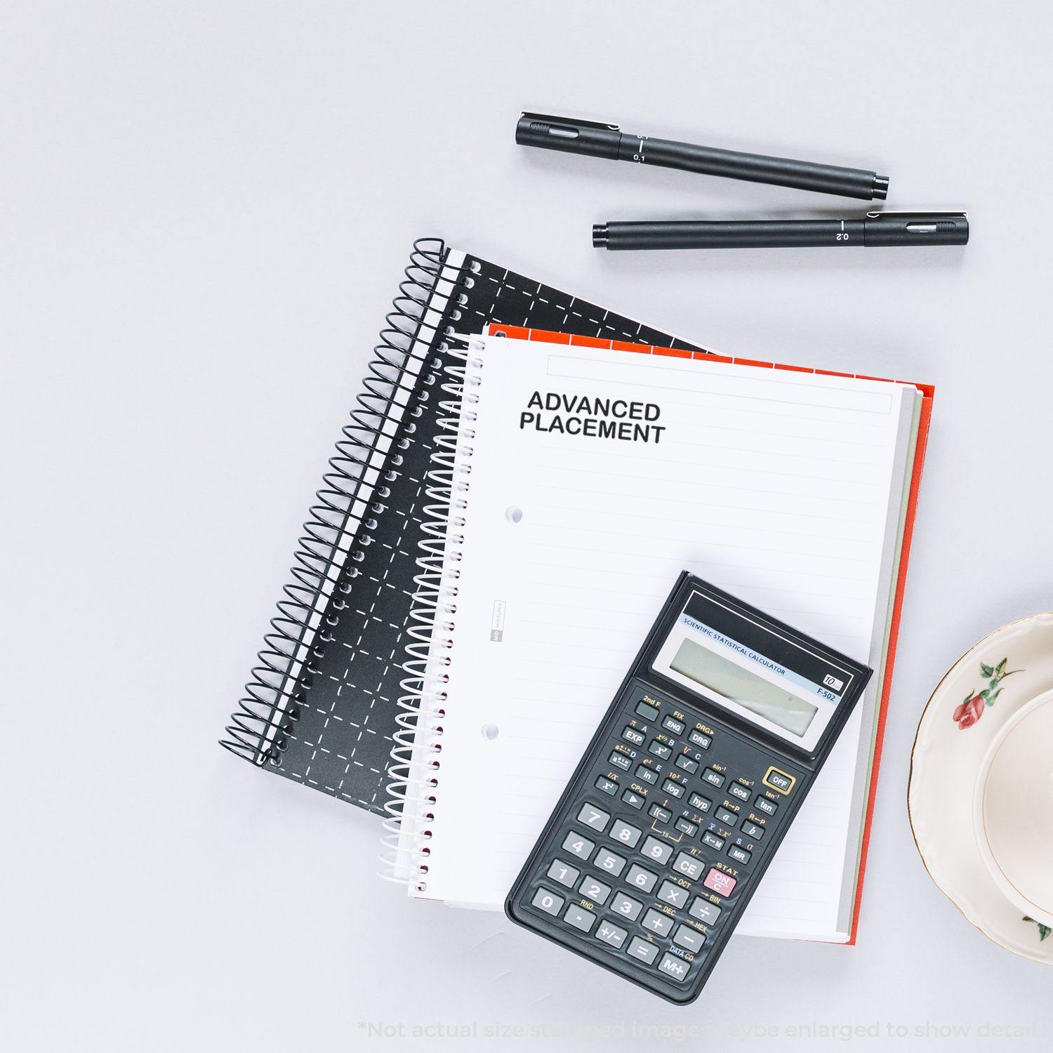 Self Inking Advanced Placement Stamp used on a notebook, with a calculator, pens, and a cup on a white surface.