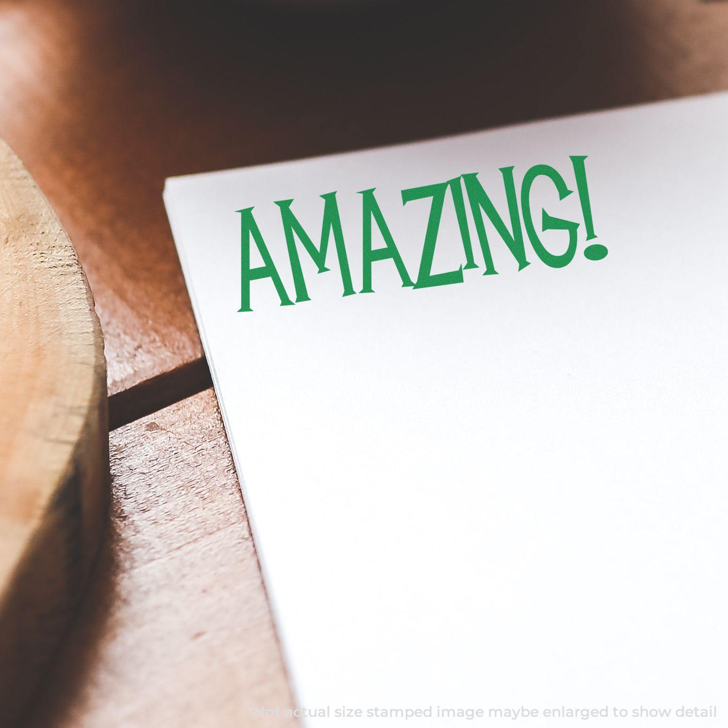 A piece of paper stamped with AMAZING! in green ink using the Large Pre-Inked Amazing Stamp, placed on a wooden surface.