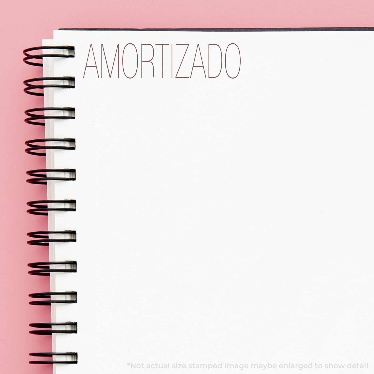 Large Self Inking Amortizado Stamp used on a white spiral notebook with a pink background.