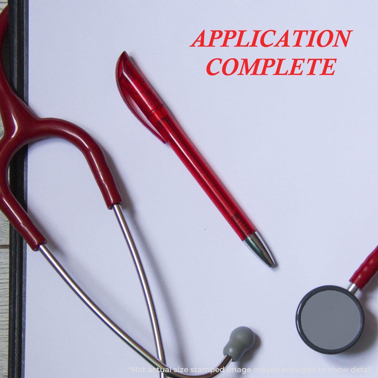 Self Inking Application Complete Stamp used on a white paper, surrounded by a red pen, stethoscope, and clipboard.