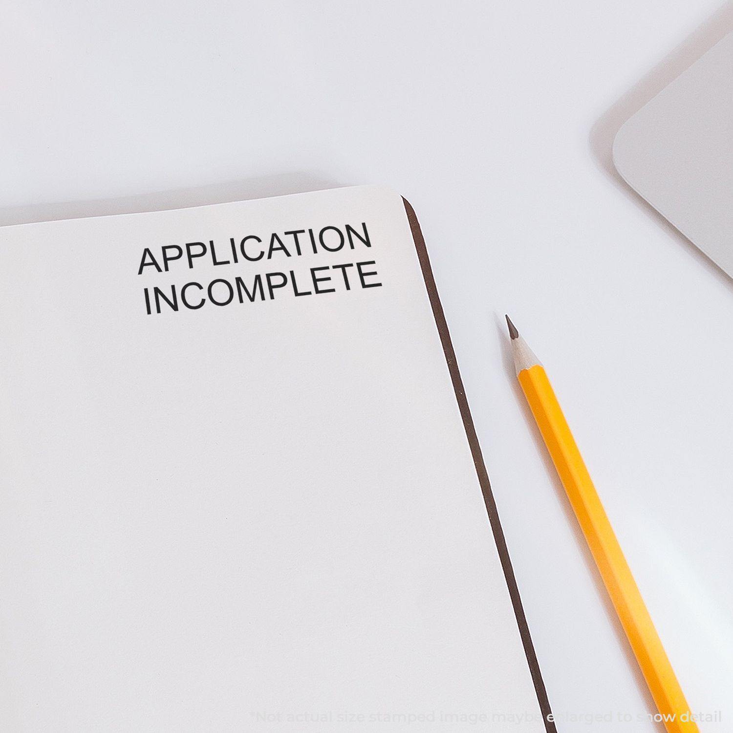 Application Incomplete rubber stamp impression on a blank page next to a yellow pencil on a white surface.