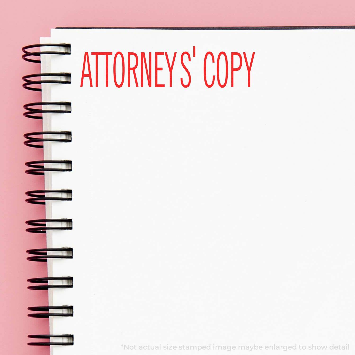 Slim Pre-Inked Attorneys' Copy Stamp imprint in red ink on a white spiral notebook against a pink background.