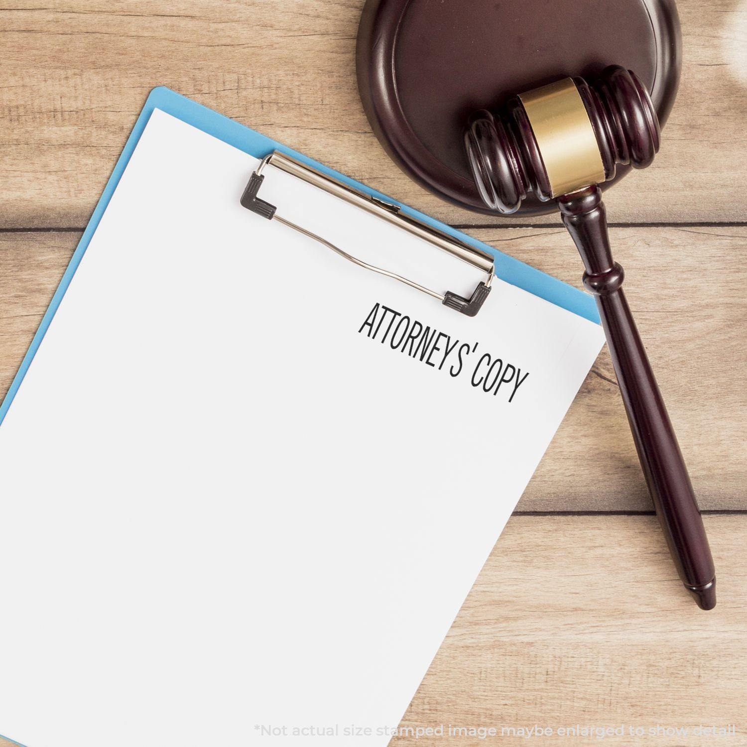 Slim Pre-Inked Attorneys' Copy Stamp on a white paper clipped to a blue clipboard, with a gavel placed beside it on a wooden surface.