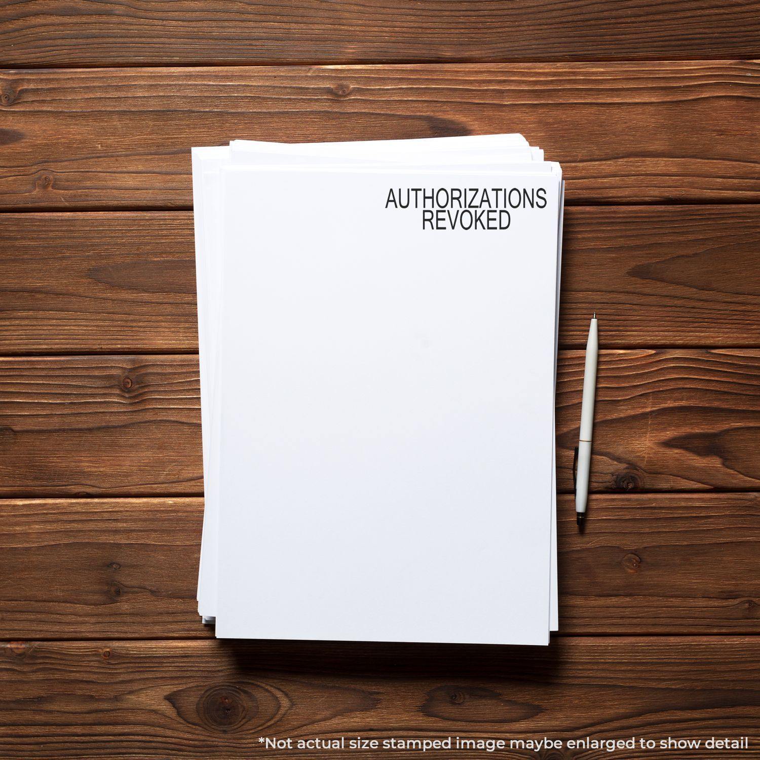 Slim Pre-Inked Authorizations Revoked Stamp used on a stack of white papers with a pen on a wooden desk.