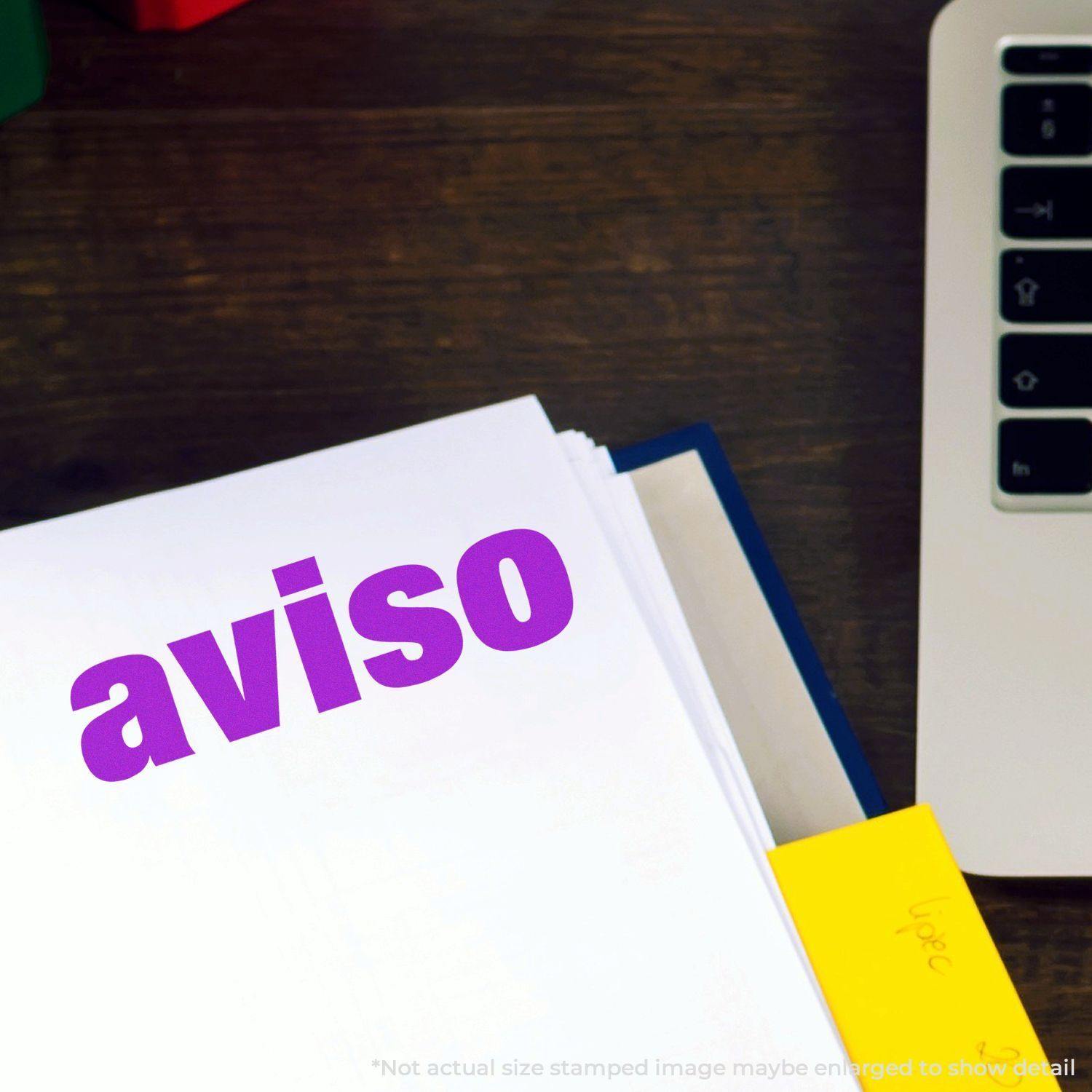 Aviso rubber stamp imprint in purple ink on a white paper, placed next to a laptop and a yellow sticky note.