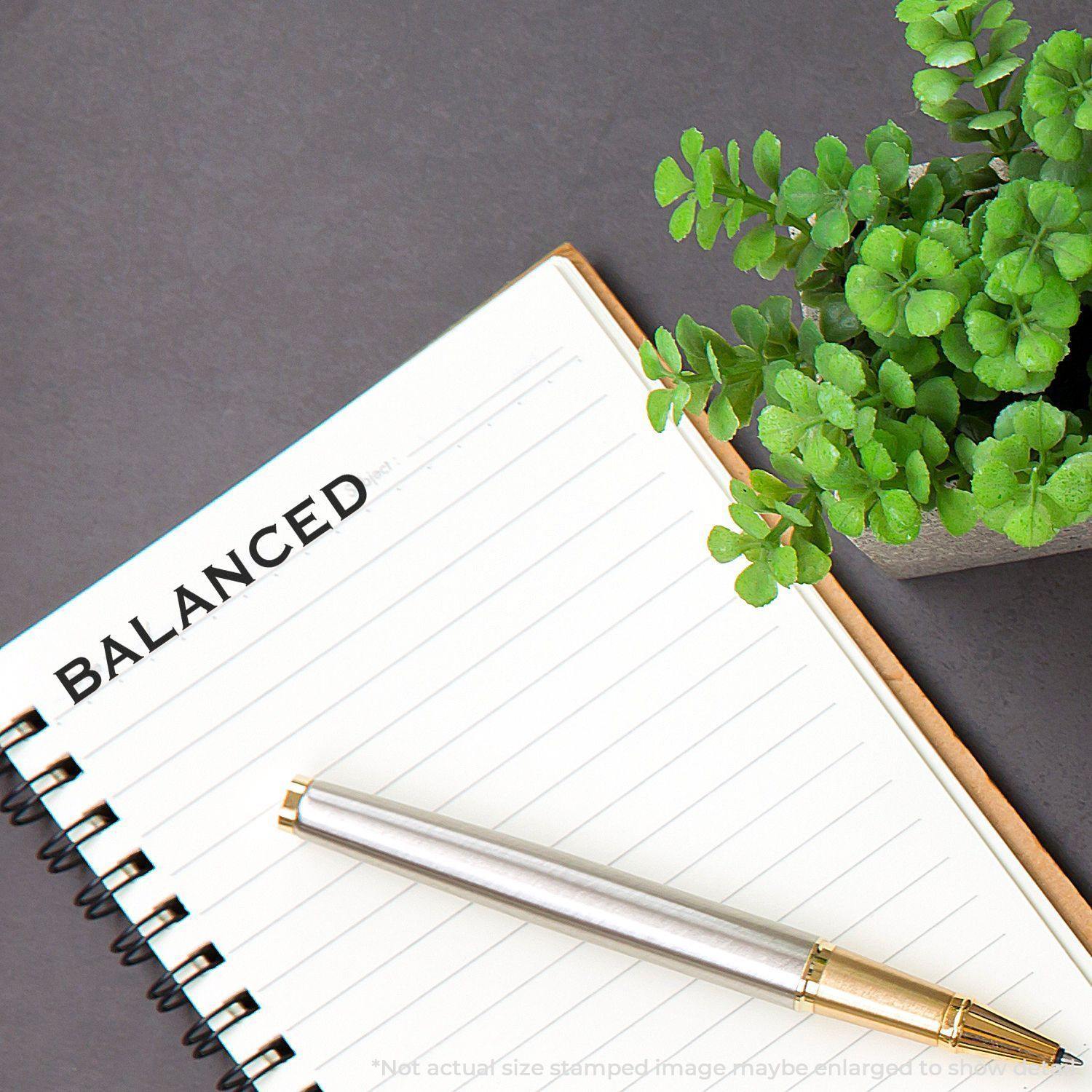 Large Pre-Inked Balanced Stamp used on a notebook page with a pen and a potted plant nearby.