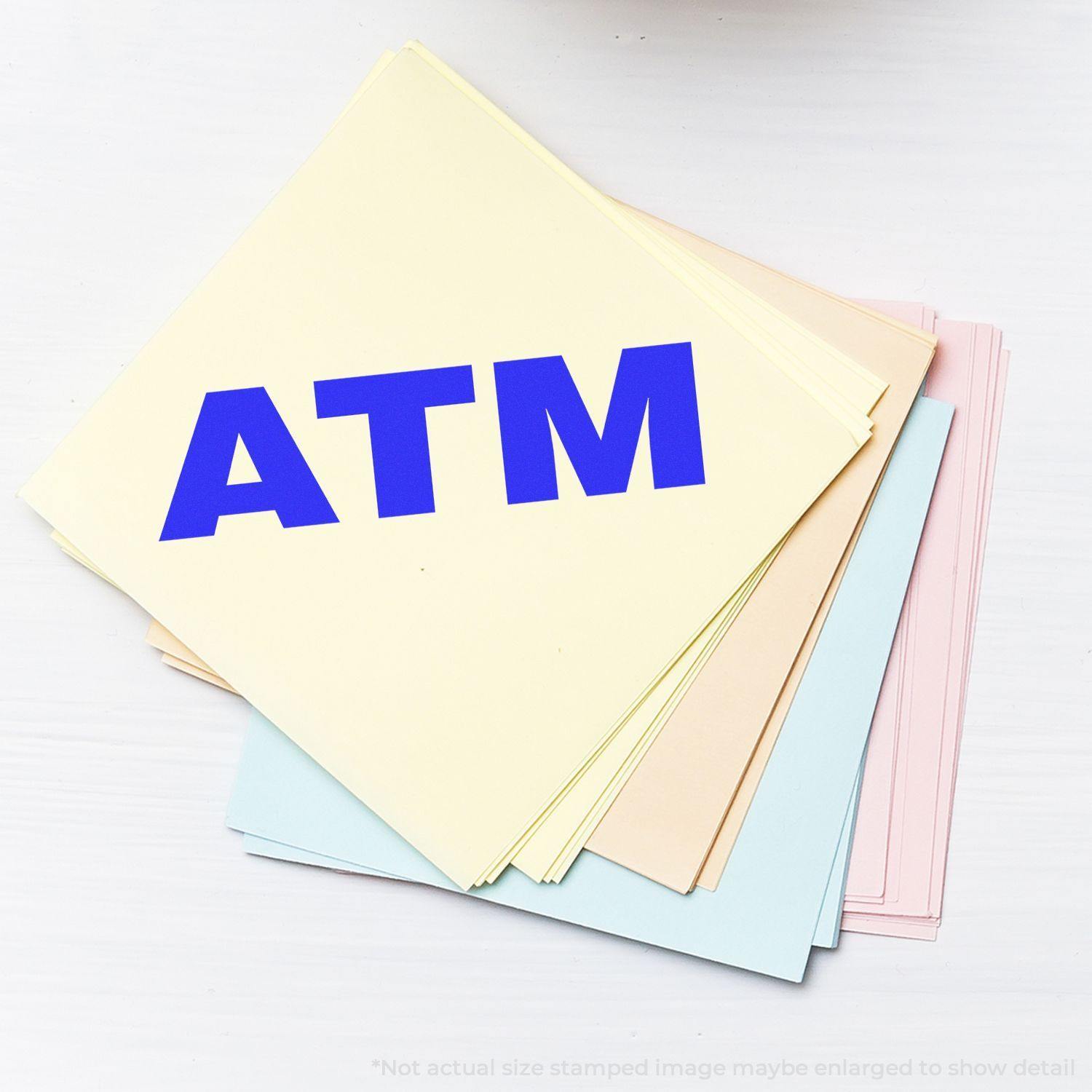 Large ATM Rubber Stamp used on a stack of pastel-colored papers, displaying a bold blue ATM imprint.