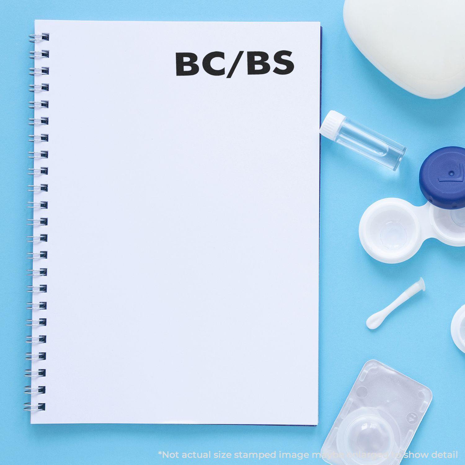 Slim Pre-Inked BC/BS Stamp used on a white spiral notebook, surrounded by medical supplies on a blue background.