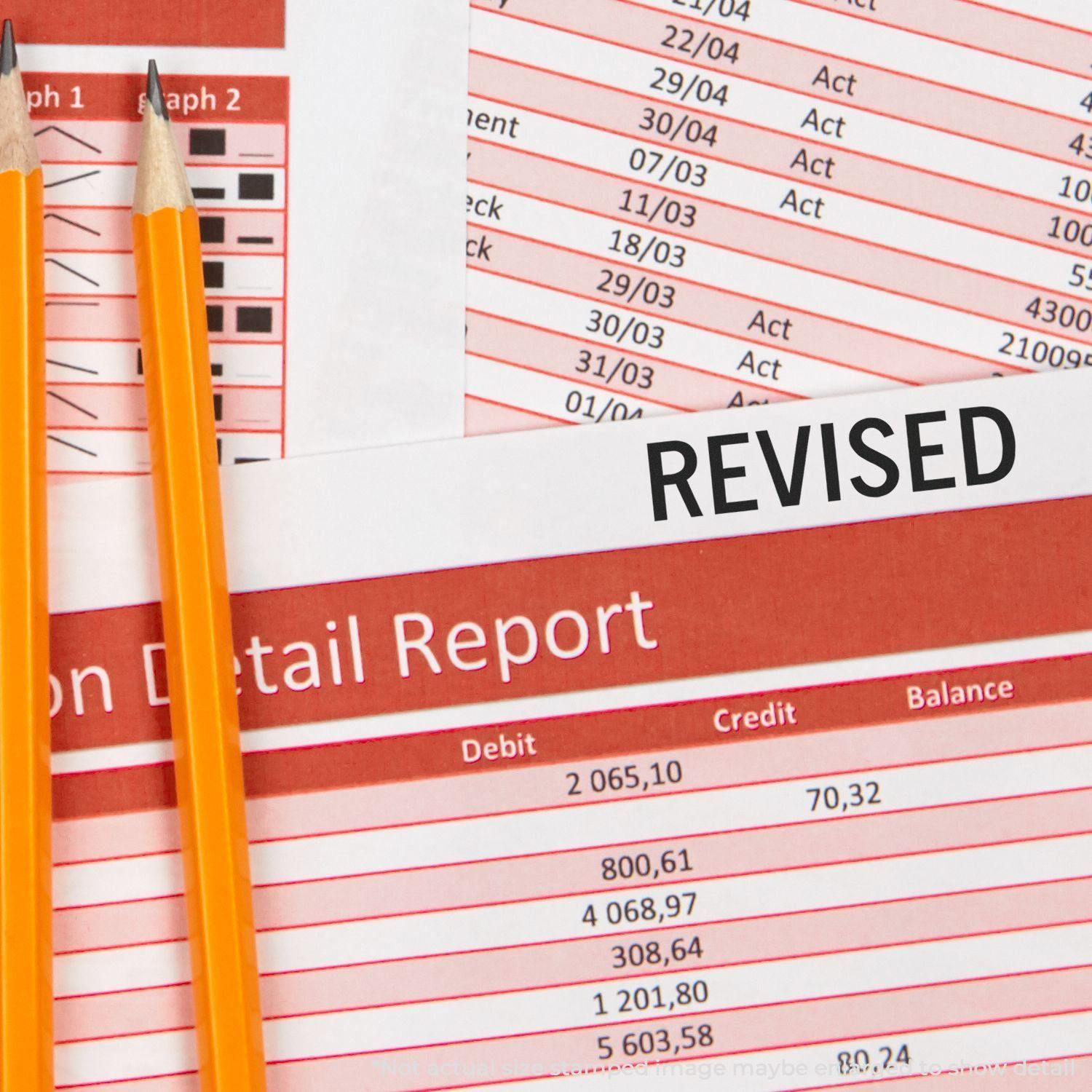 Two pencils on a financial report stamped with a black Revised Rubber Stamp indicating changes or updates to the document.