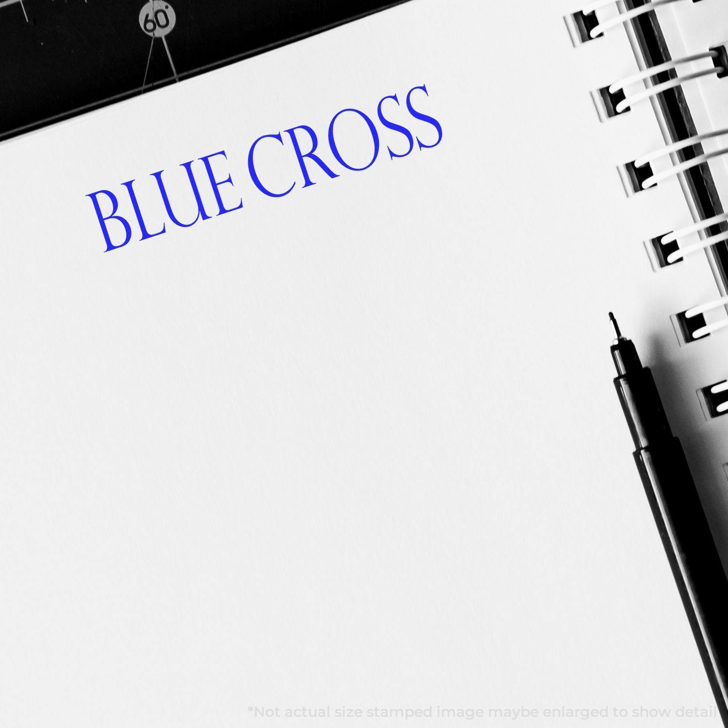 Blue Cross rubber stamp impression on white paper with a black pen and a spiral notebook in the background.