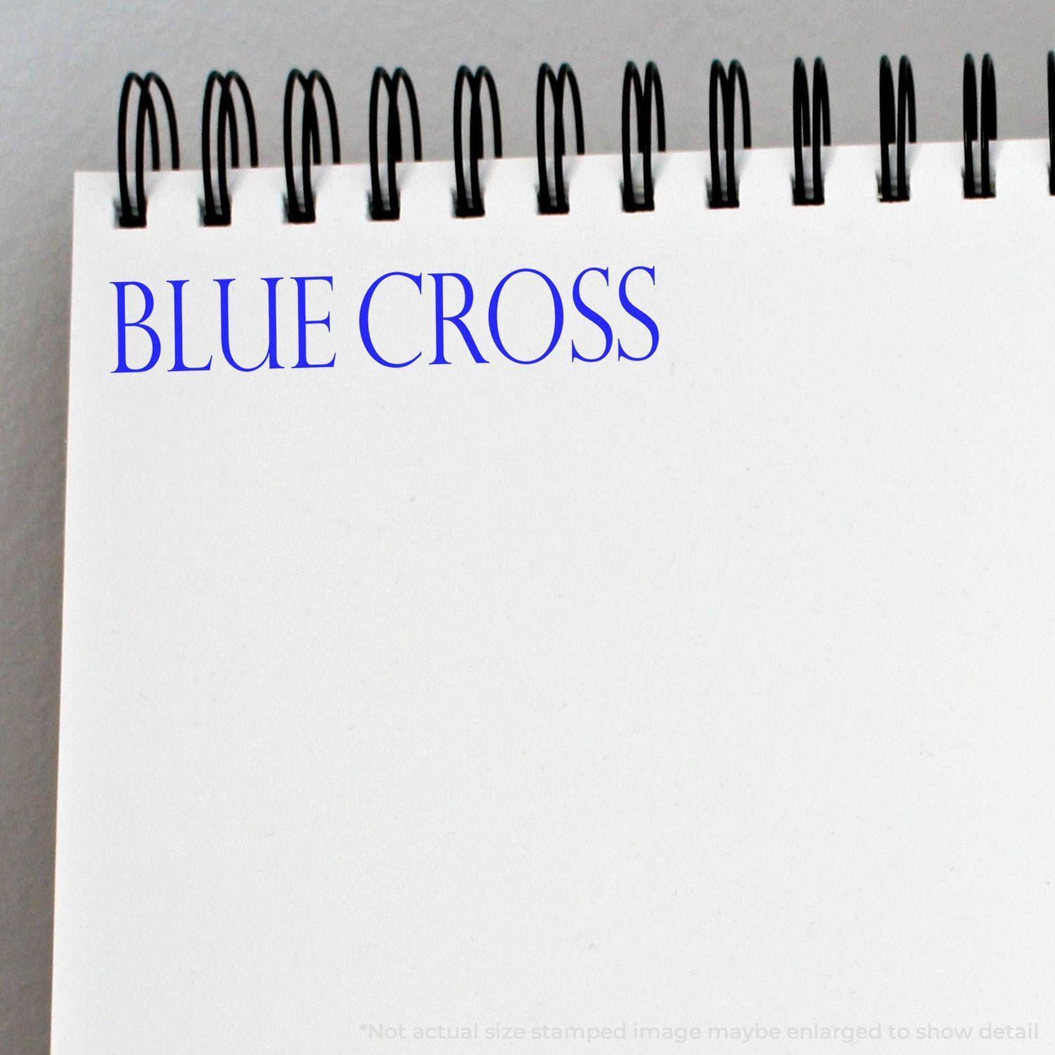 A notebook with a spiral binding has a Blue Cross rubber stamp impression in blue ink on the top left corner of the page.