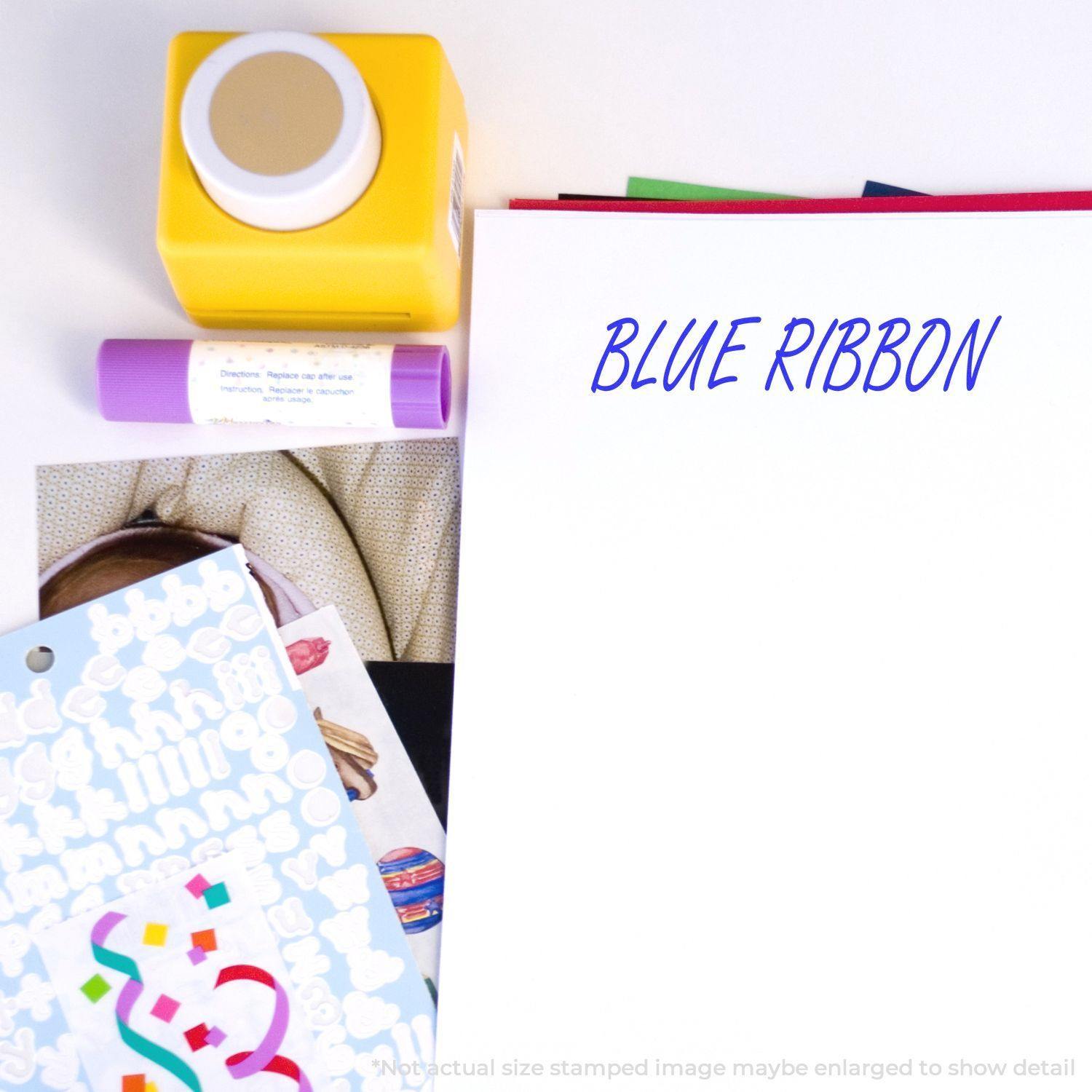 Blue Ribbon Rubber Stamp in use on white paper, surrounded by colorful stickers, a yellow stamp tool, and a purple marker.