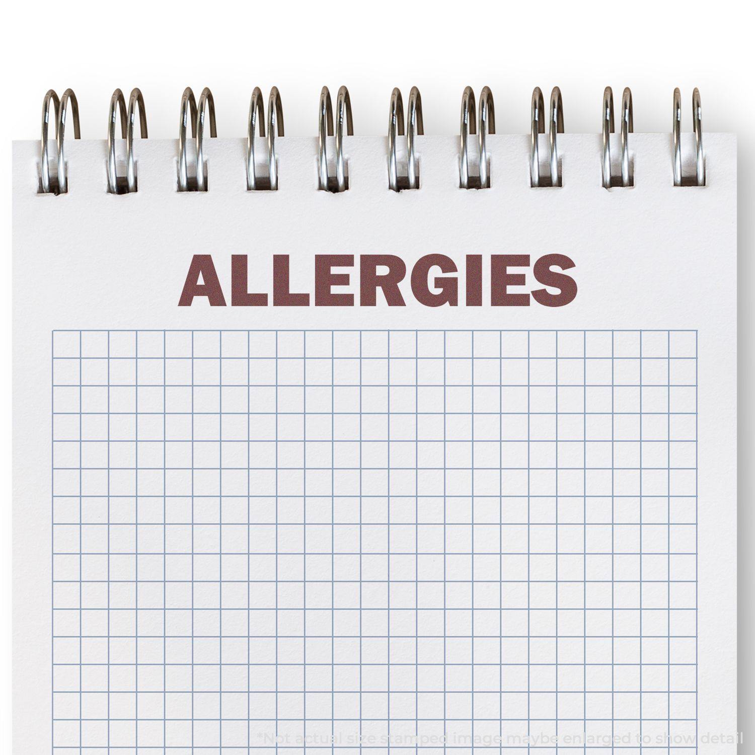 Slim Pre-Inked Bold Allergies Stamp used on a spiral notebook with a grid pattern, displaying the word ALLERGIES in bold red text.