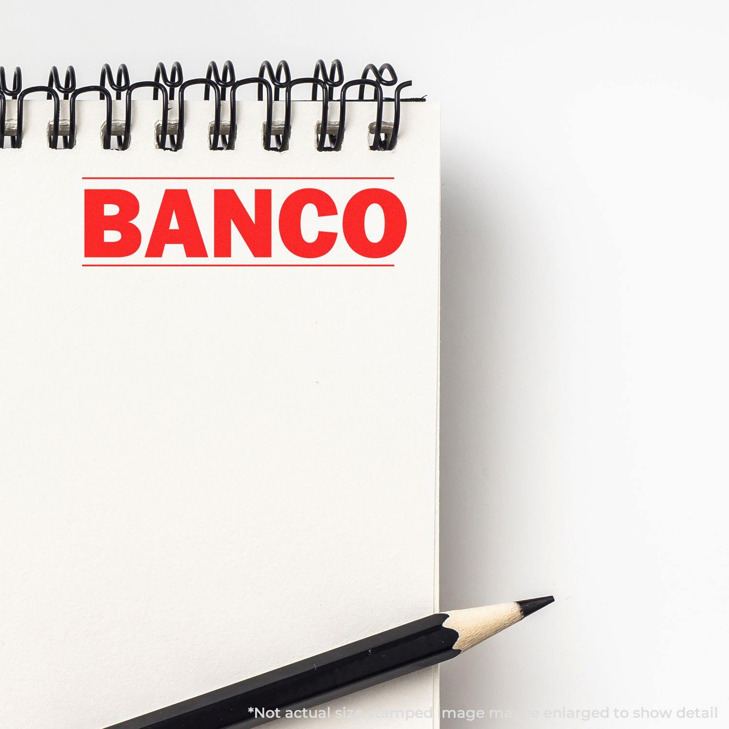 Slim Pre-Inked Bold Banco Stamp imprint in red on a white notepad with a black pencil beside it.