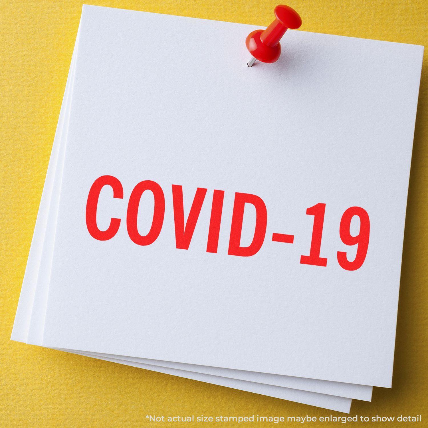 Large Self Inking Bold Covid-19 Stamp in red ink on white paper, pinned with a red pushpin on a yellow background.