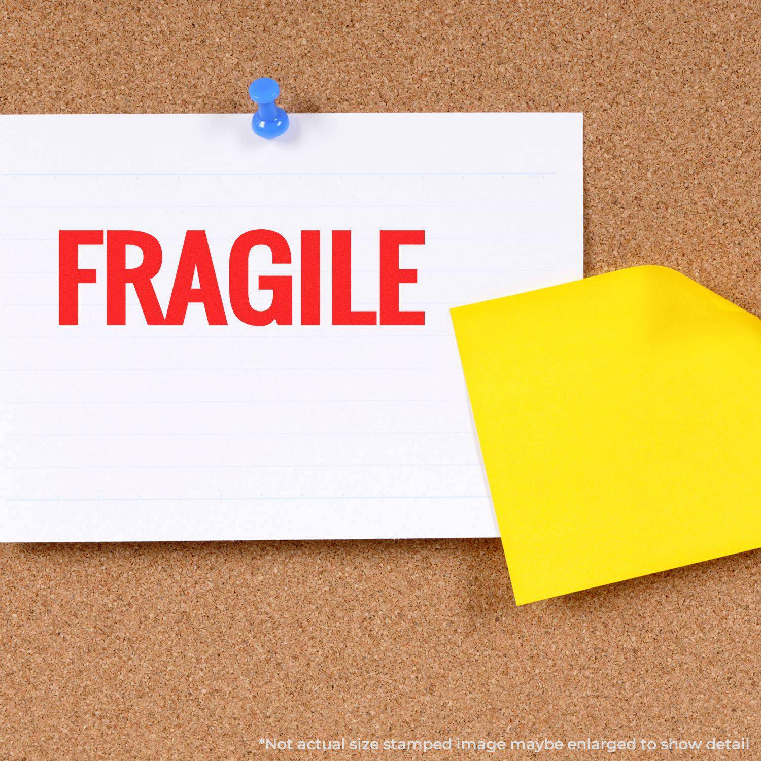 Large Self Inking Bold Fragile Stamp used on a white paper pinned to a corkboard with a blue pushpin and a yellow sticky note beside it.