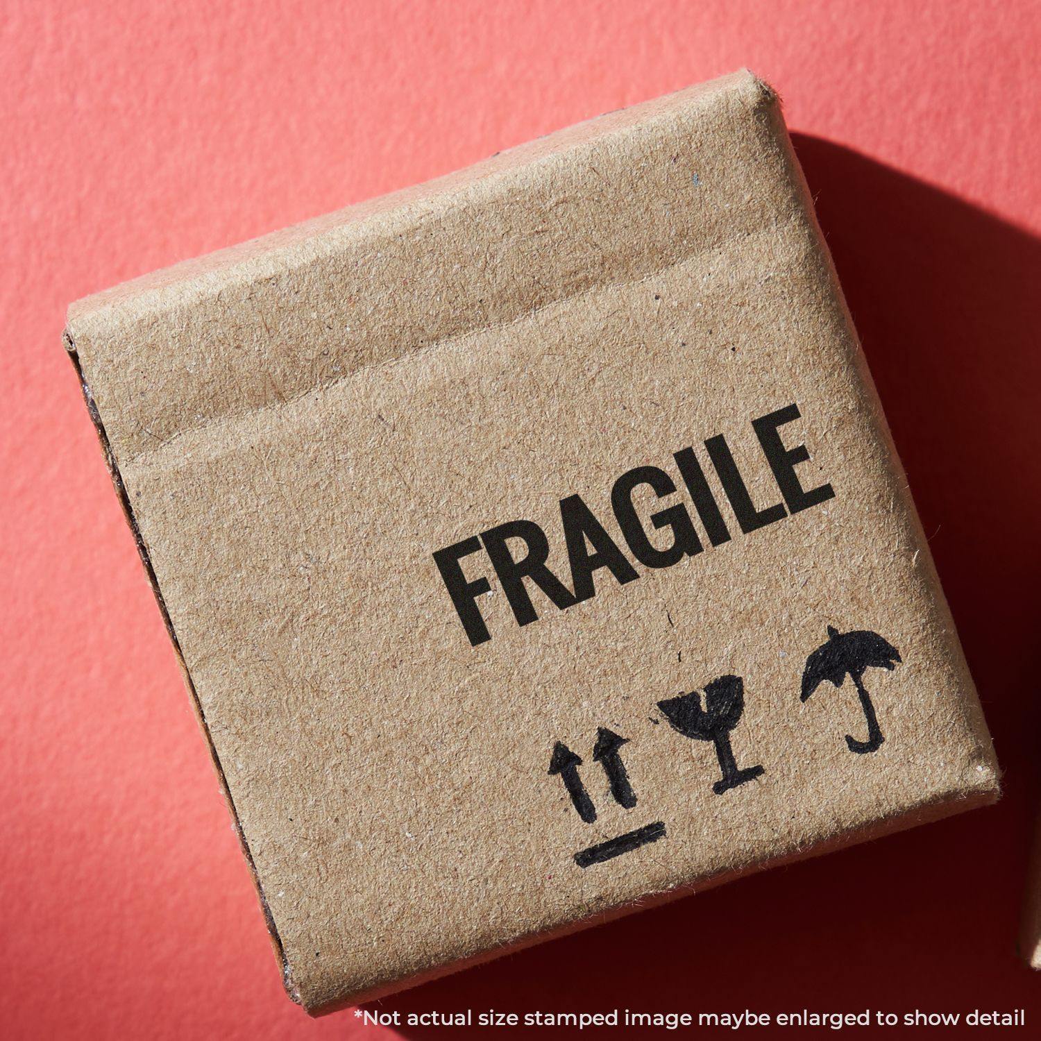 A cardboard box stamped with FRAGILE using the Large Bold Fragile Pre-Inked Stamp, placed on a red background.