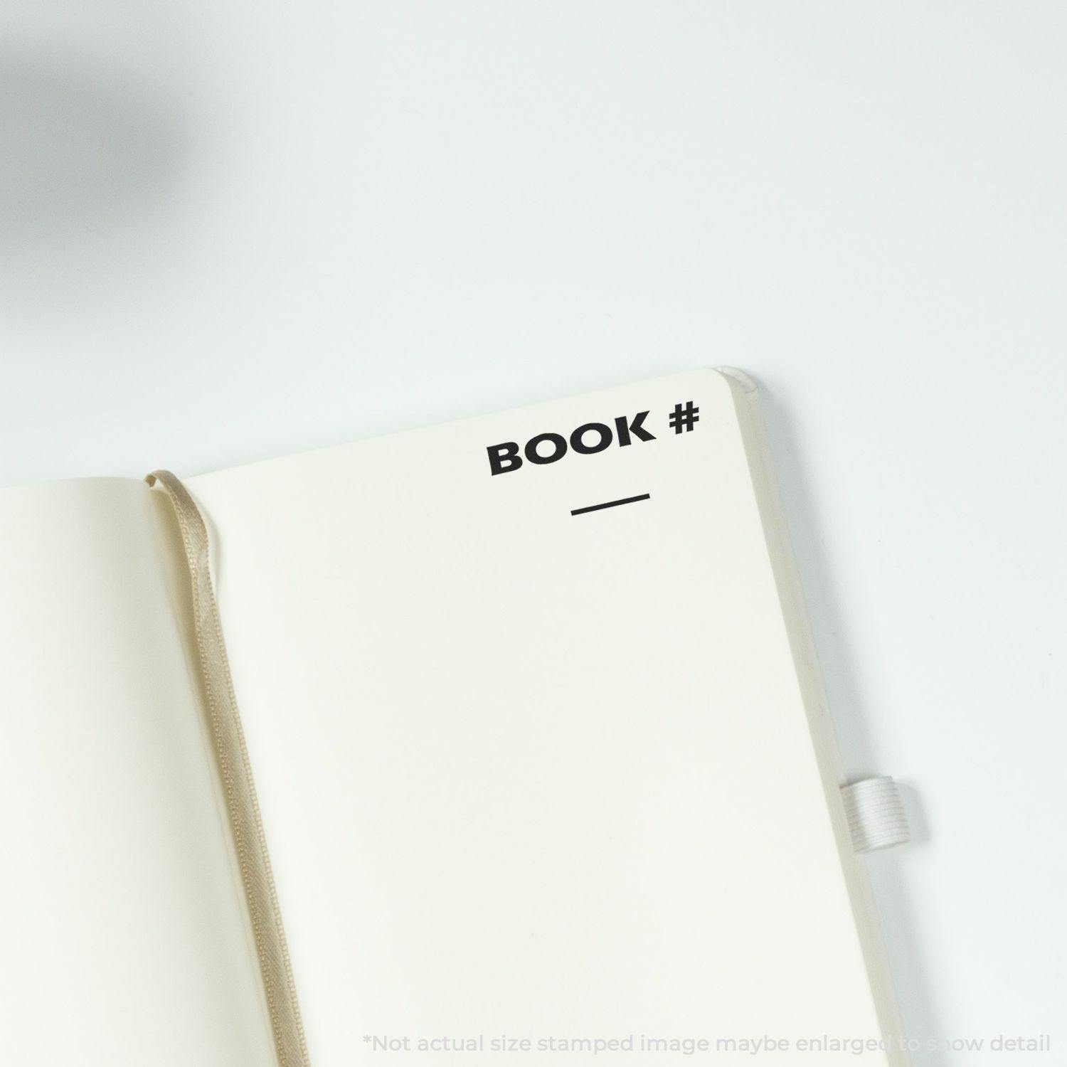 Open notebook with BOOK # stamped using the Large Self Inking Book Stamp, showing a blank line for numbering.