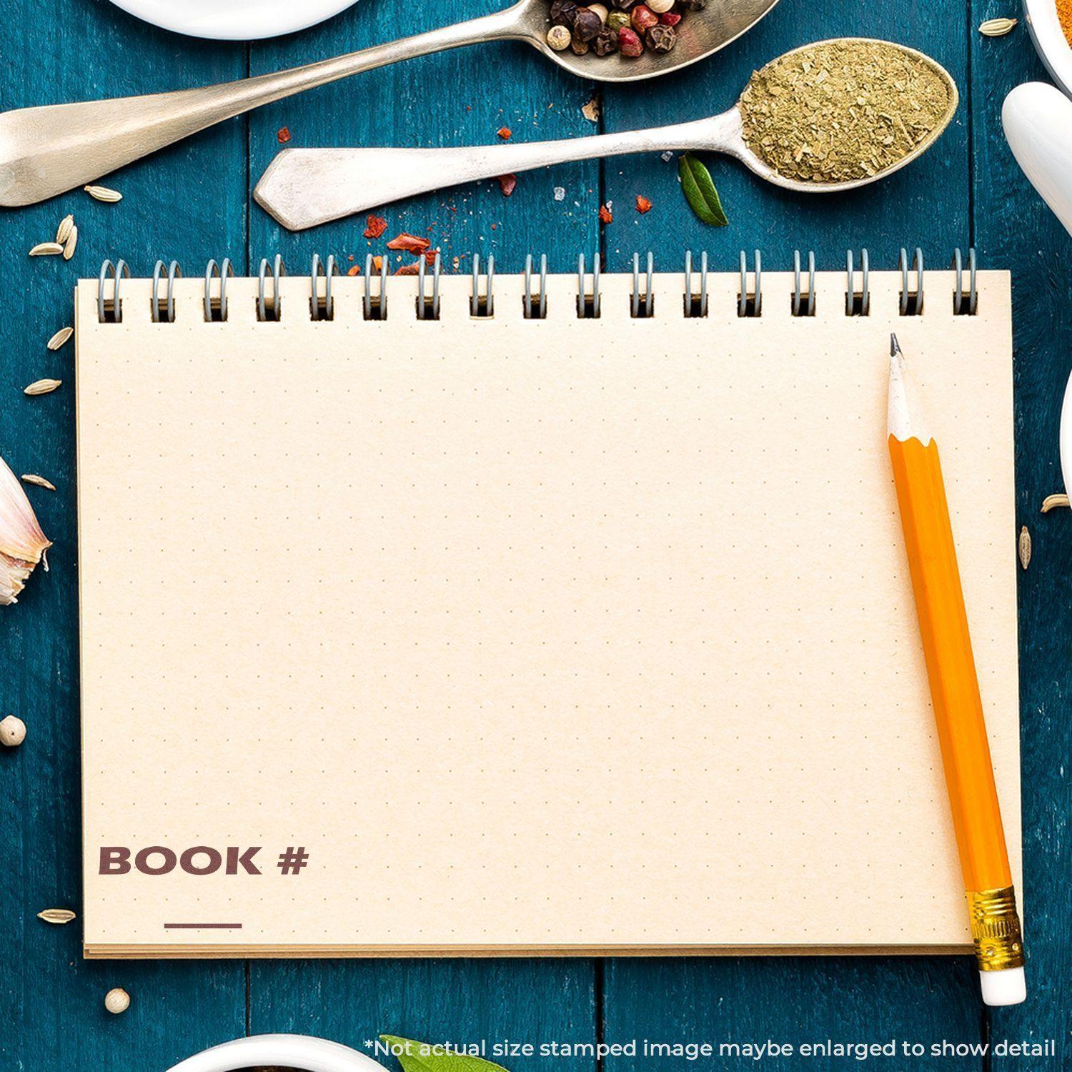 Large Pre-Inked Book Stamp used on an open notebook with a pencil on a blue wooden table, surrounded by spices and herbs.