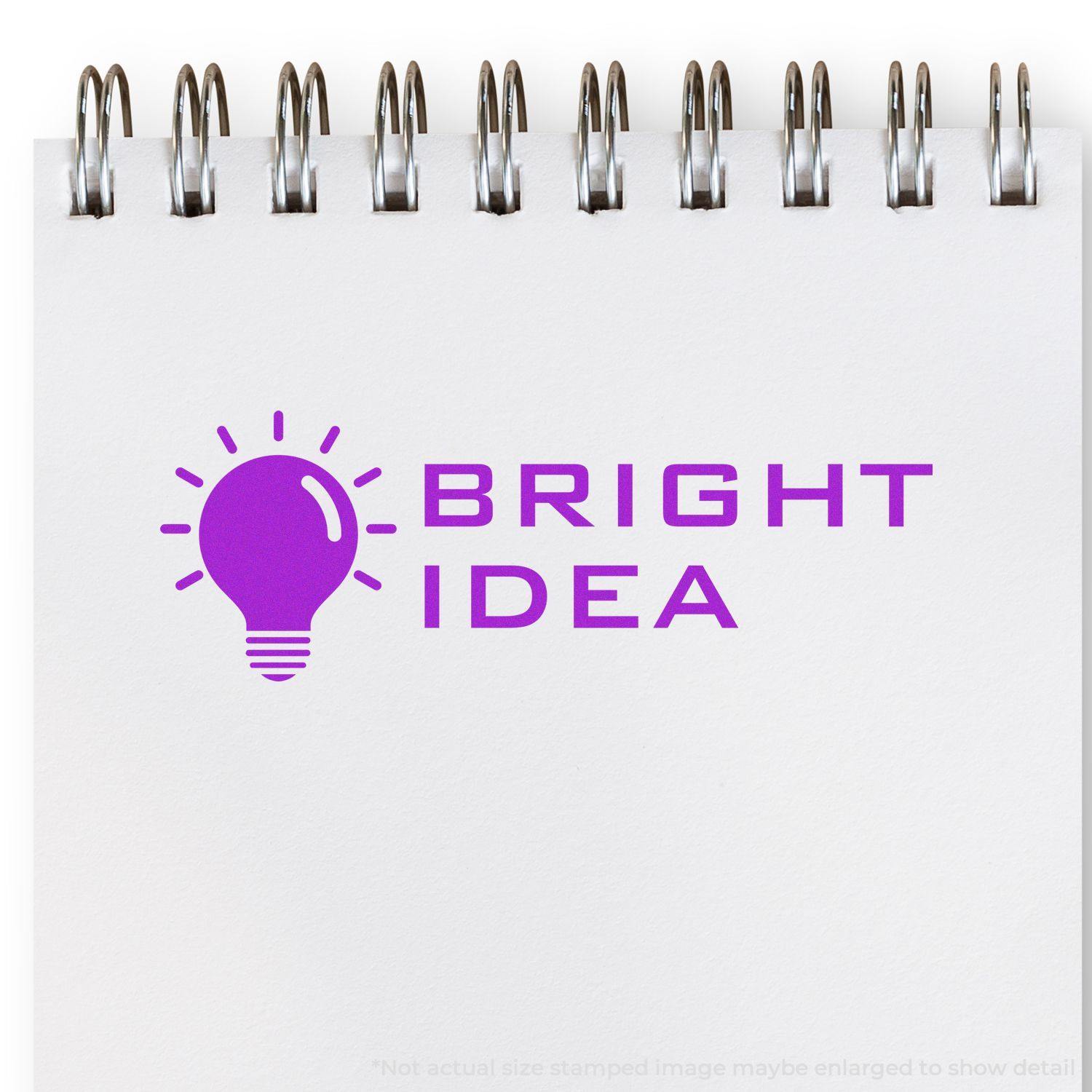 A self-inking stamp with a stamped image showing how the text "BRIGHT IDEA" in a tech-style font with an image of a bright lightbulb on the left side of the text is displayed after stamping.