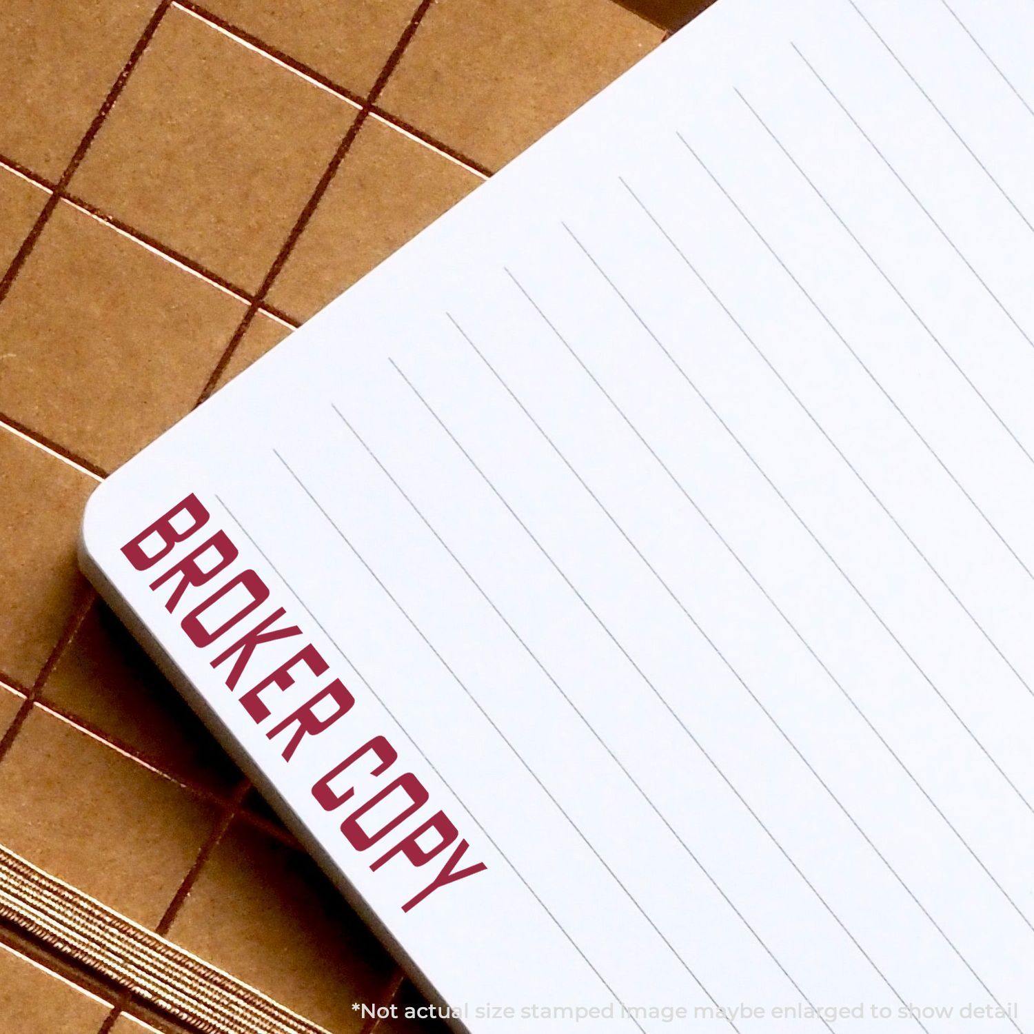 Broker Copy rubber stamp impression in red ink on the top corner of a lined notepad, placed on a brown grid-patterned surface.