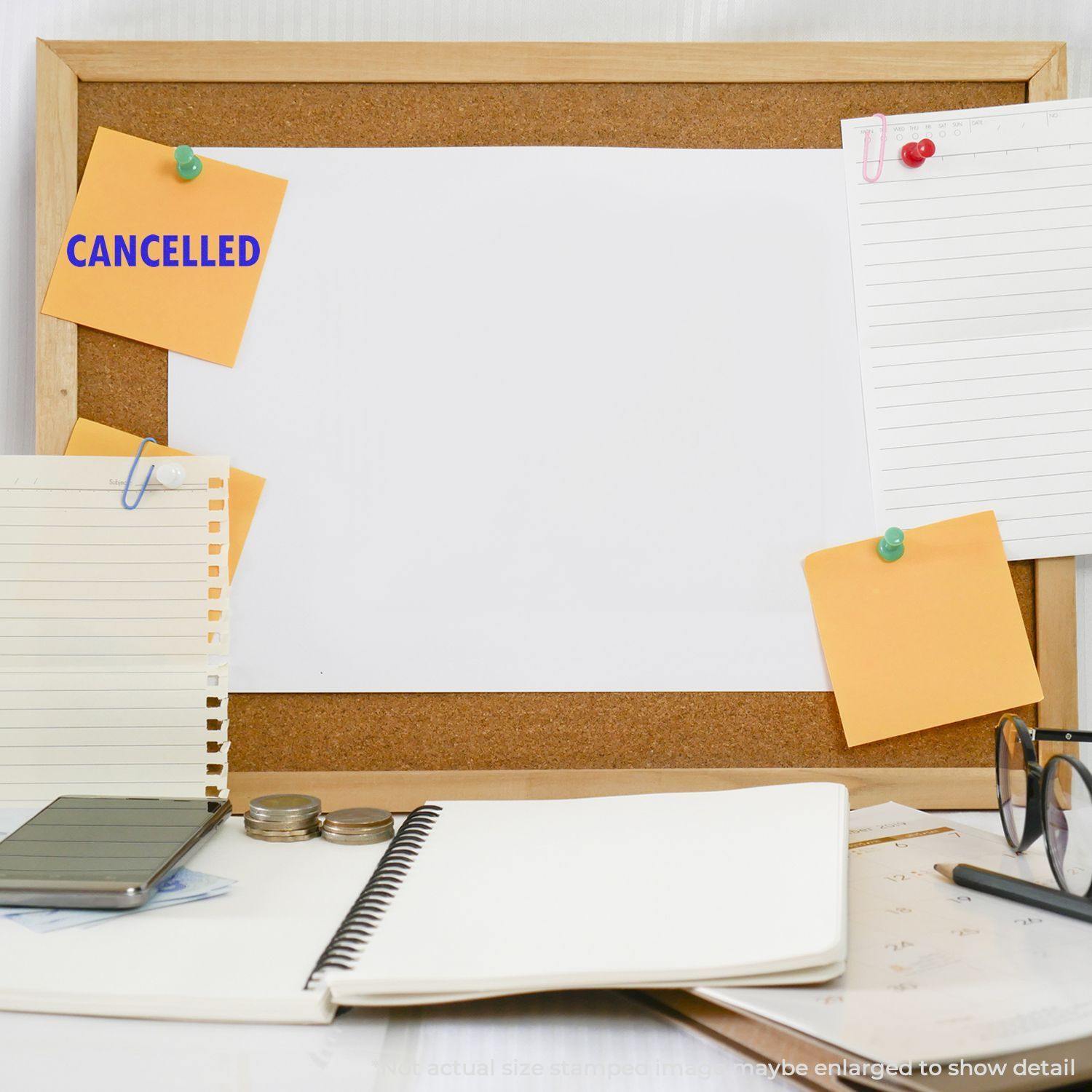 Large Self Inking Cancelled Stamp used on a yellow sticky note pinned to a corkboard, surrounded by notebooks, papers, glasses, and coins on a desk.