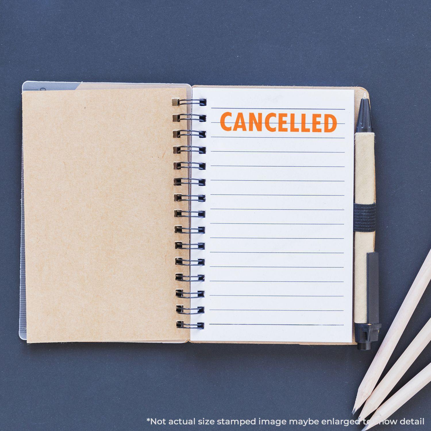 Open notebook with CANCELLED rubber stamp in orange ink on lined page, surrounded by pencils and a pen.