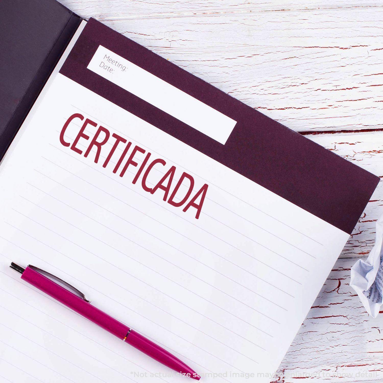 Self Inking Certificada Stamp in red ink on a notebook page with a pink pen beside it on a white wooden surface.