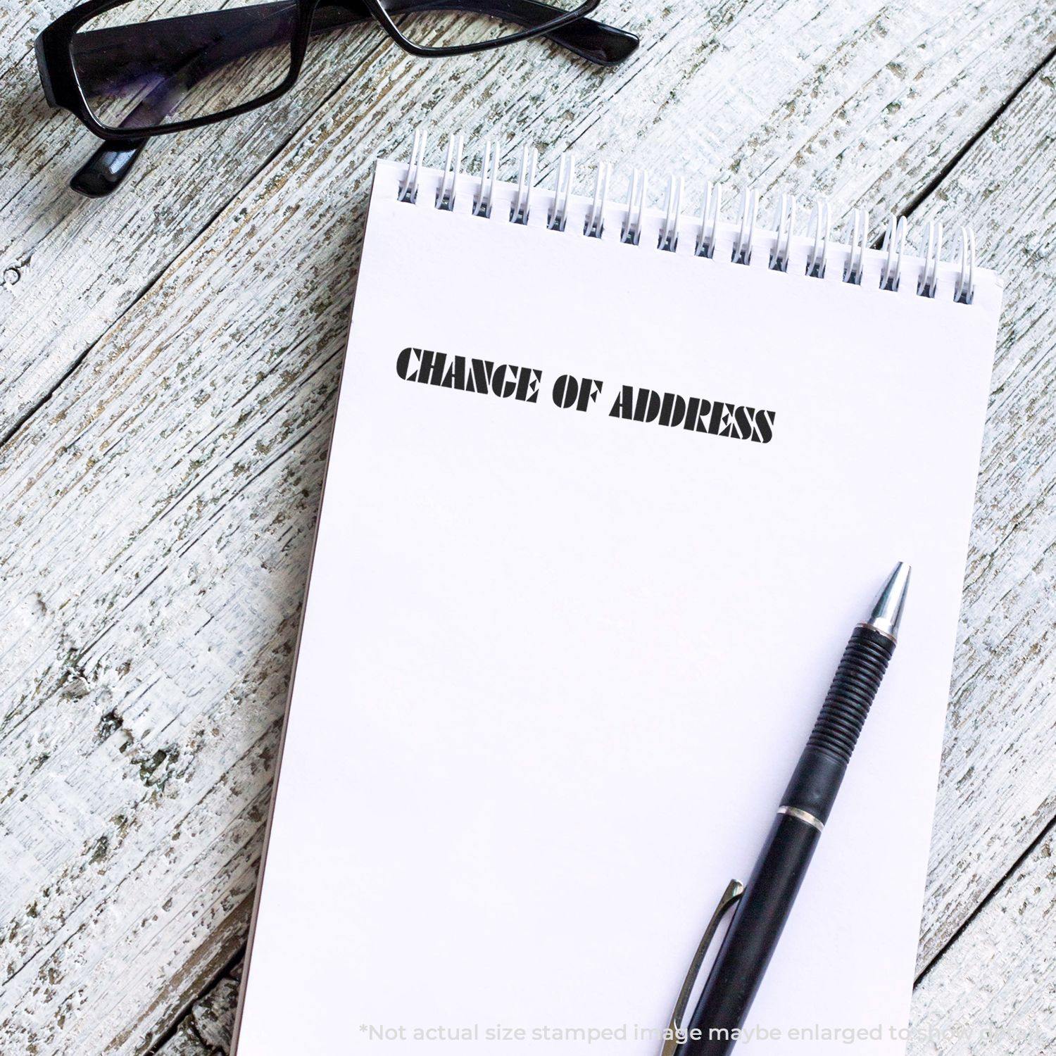 Change Of Address Rubber Stamp used on a notepad with a pen and glasses placed on a wooden surface.