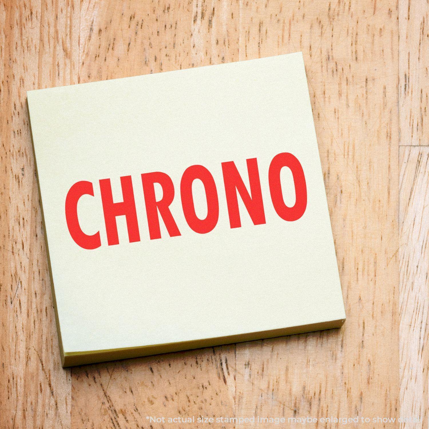 Self Inking Chrono Stamp imprint on a yellow sticky note with a wooden background. The word "CHRONO" is stamped in bold red letters.