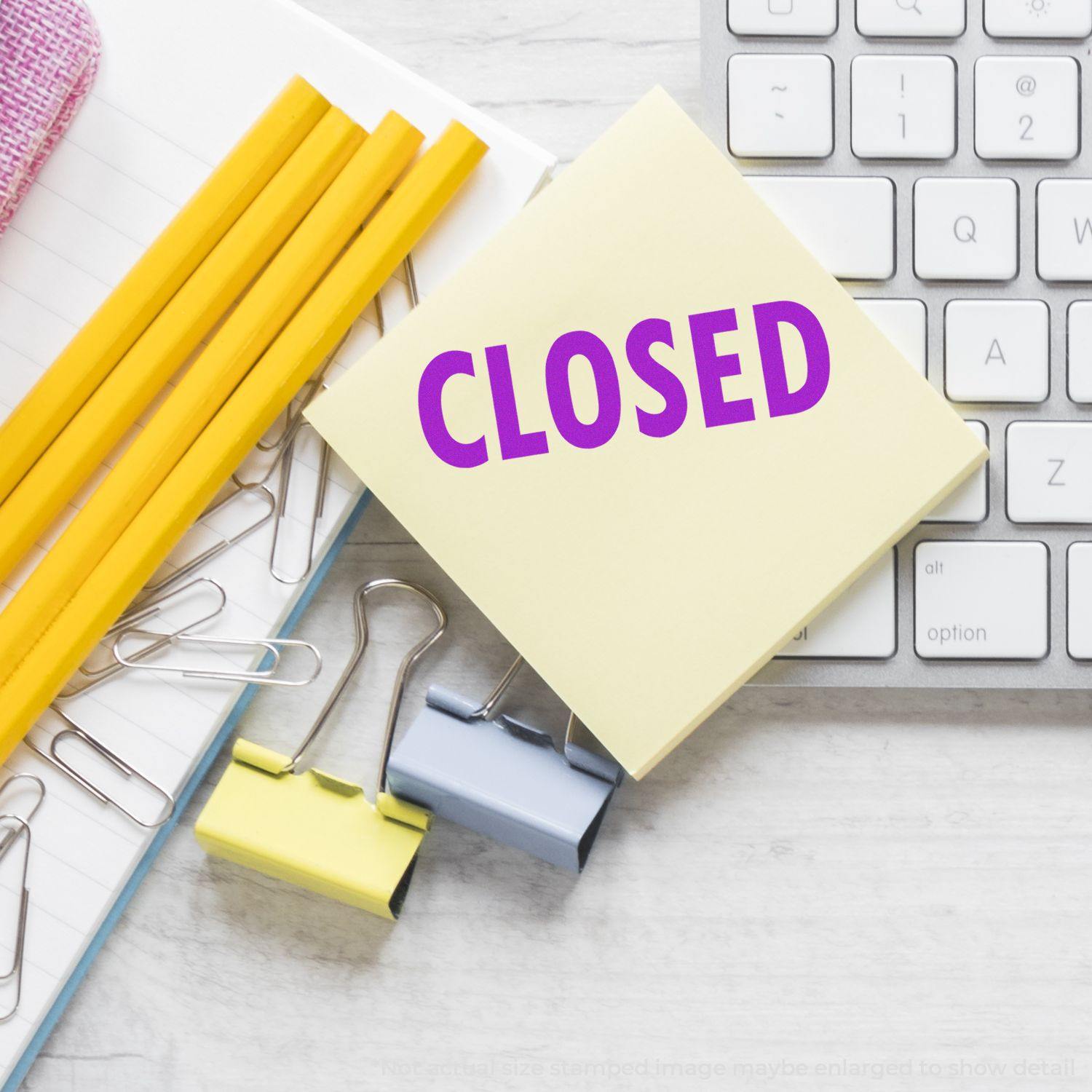 Large Self Inking Closed Stamp on a desk with pencils, paper clips, binder clips, and a keyboard in the background.